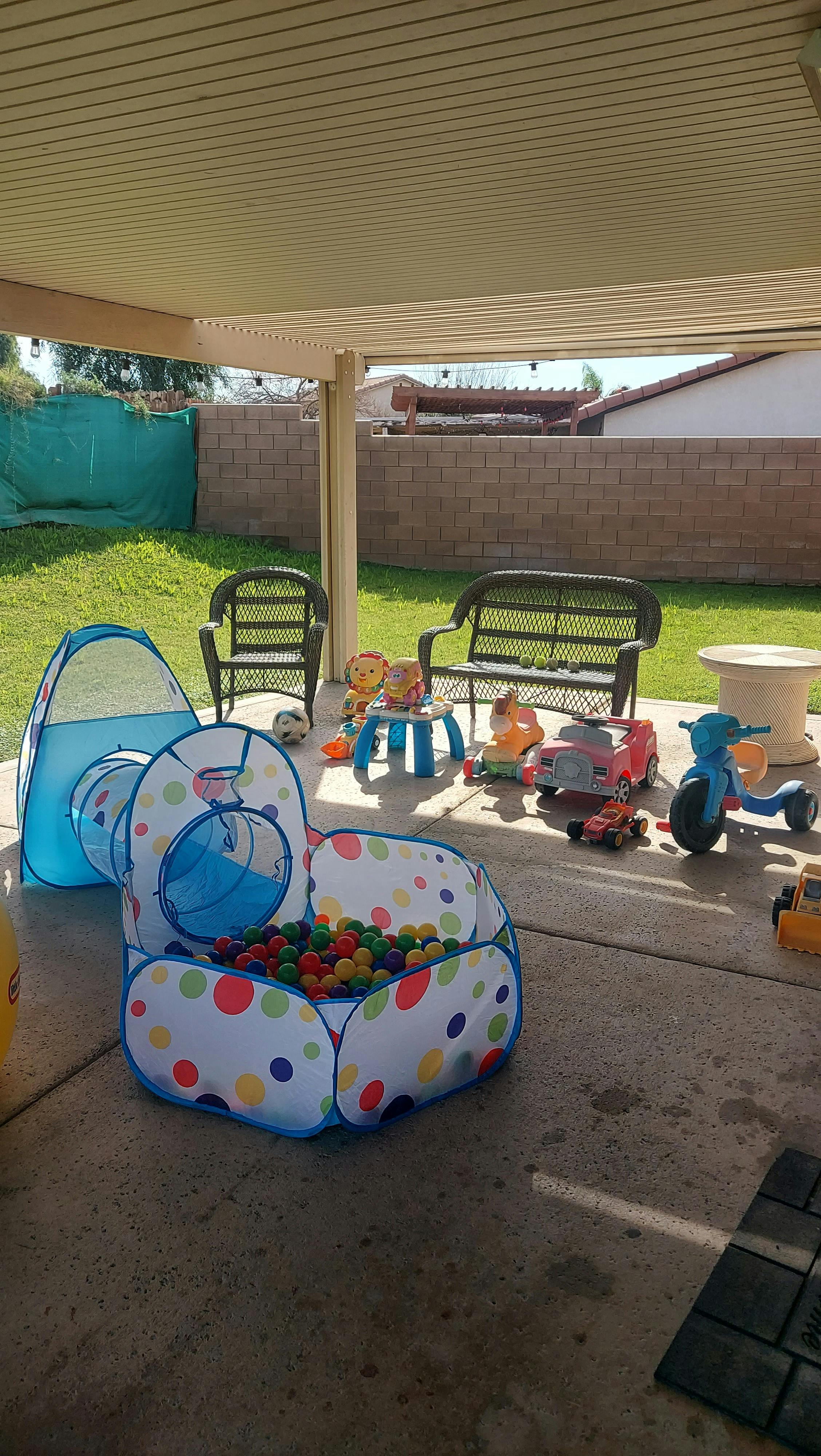 Children's ball pit with tunnel attachment and various toys on a patio
