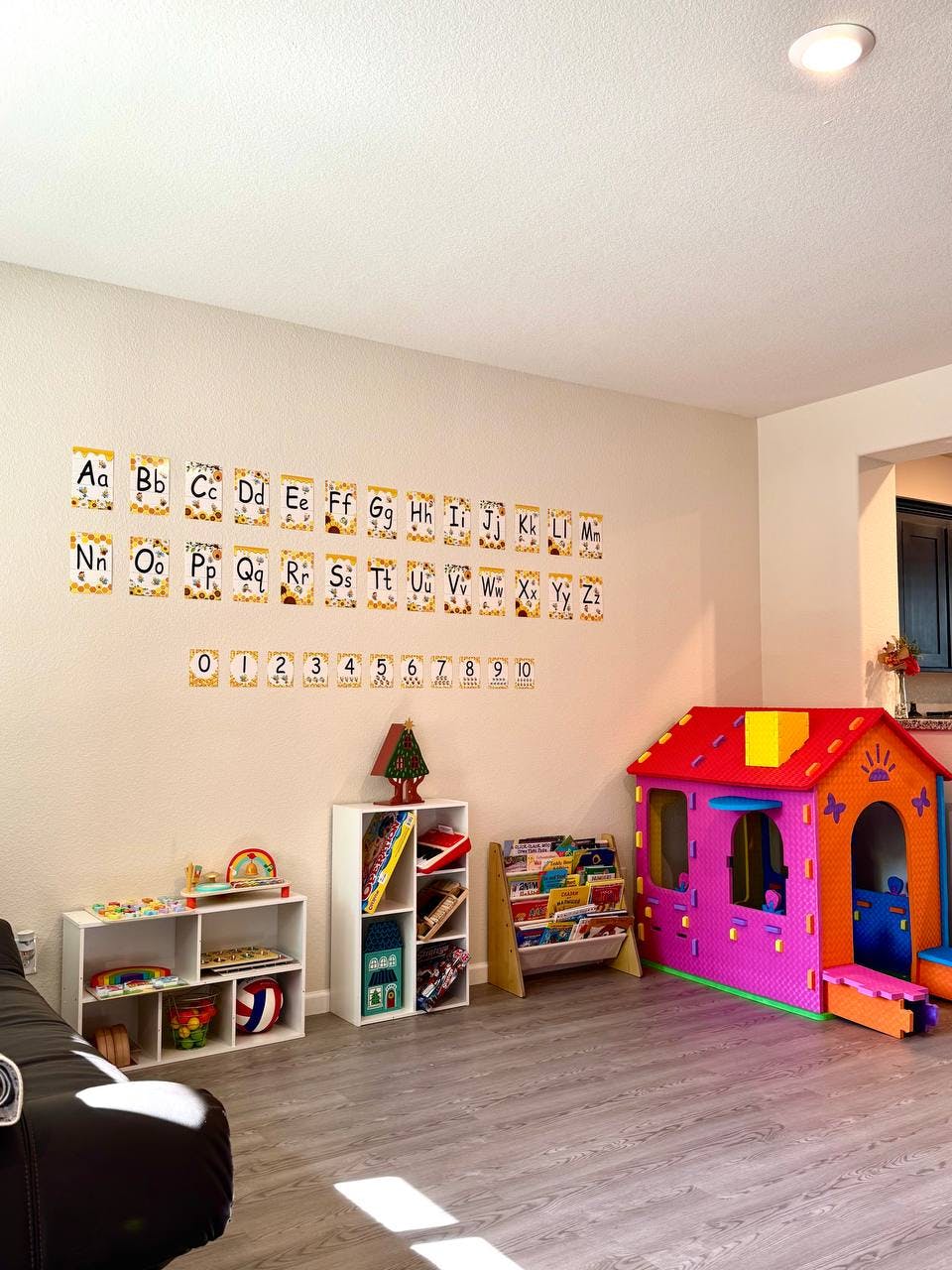 Playroom with alphabet and number charts on the wall, shelves with toys, and a playhouse