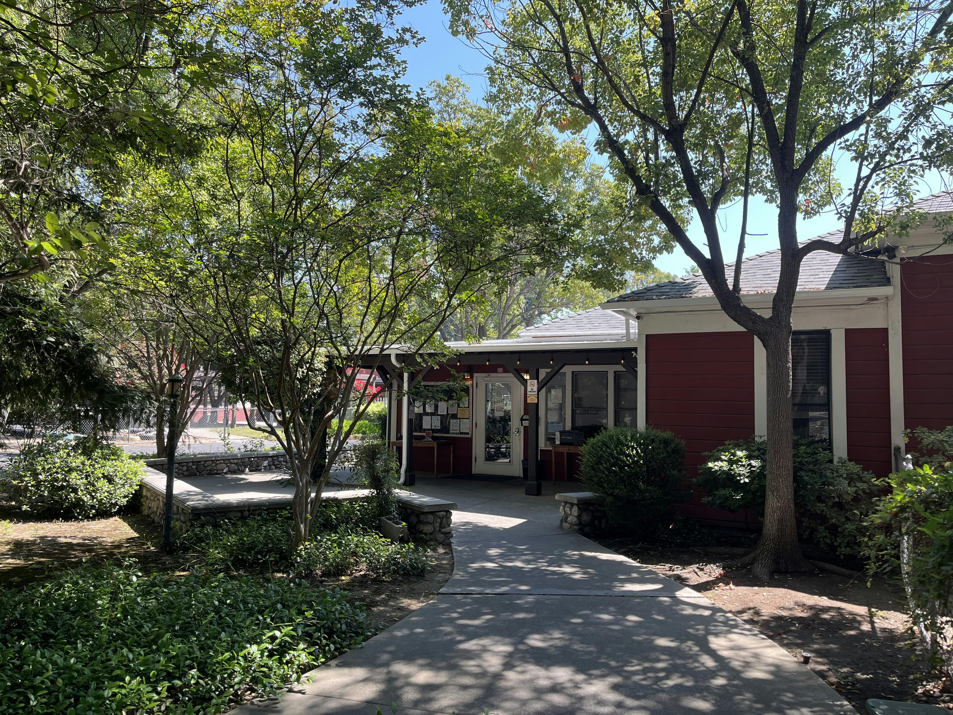 Red building surrounded by trees and green bushes, with a paved walkway leading to its entrance