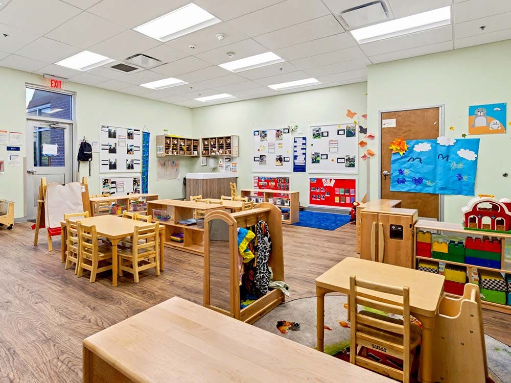 Empty children's classroom with small wooden tables and chairs, and play areas