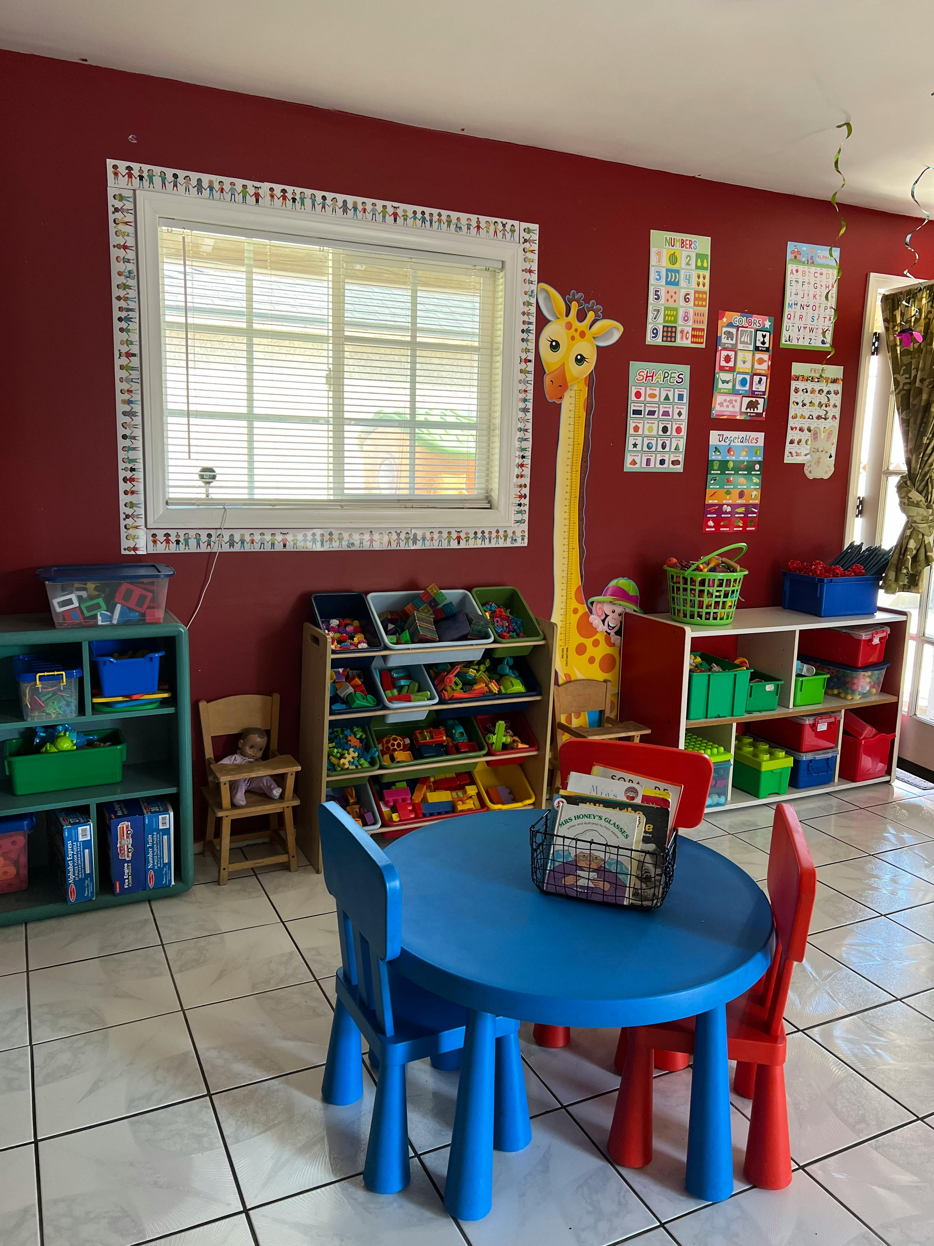 Playroom with a blue table and chairs, toy shelves, and a window