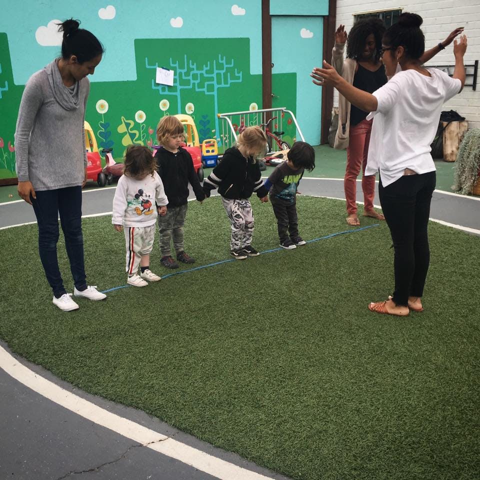 Two people and four children holding hands in a line on artificial grass