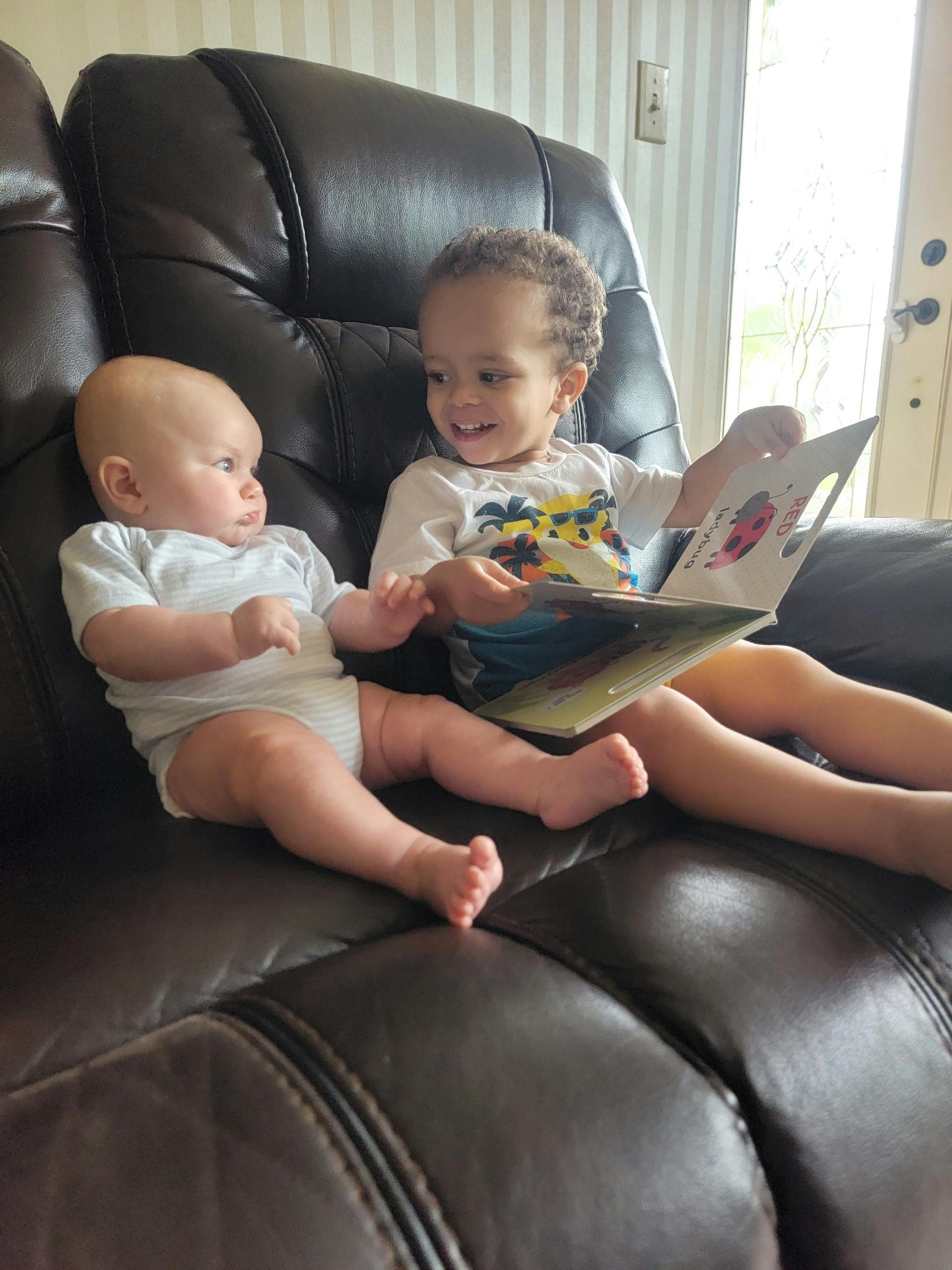 Two children sitting on a couch, one holding a book