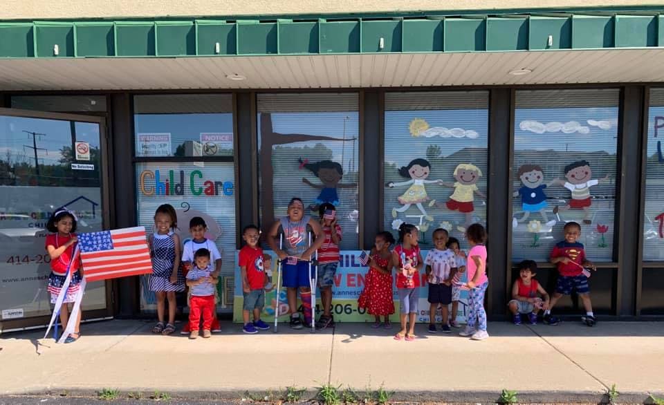 Group of children standing in front of a building, one holding an American flag