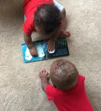 Two babies on floor looking at open book