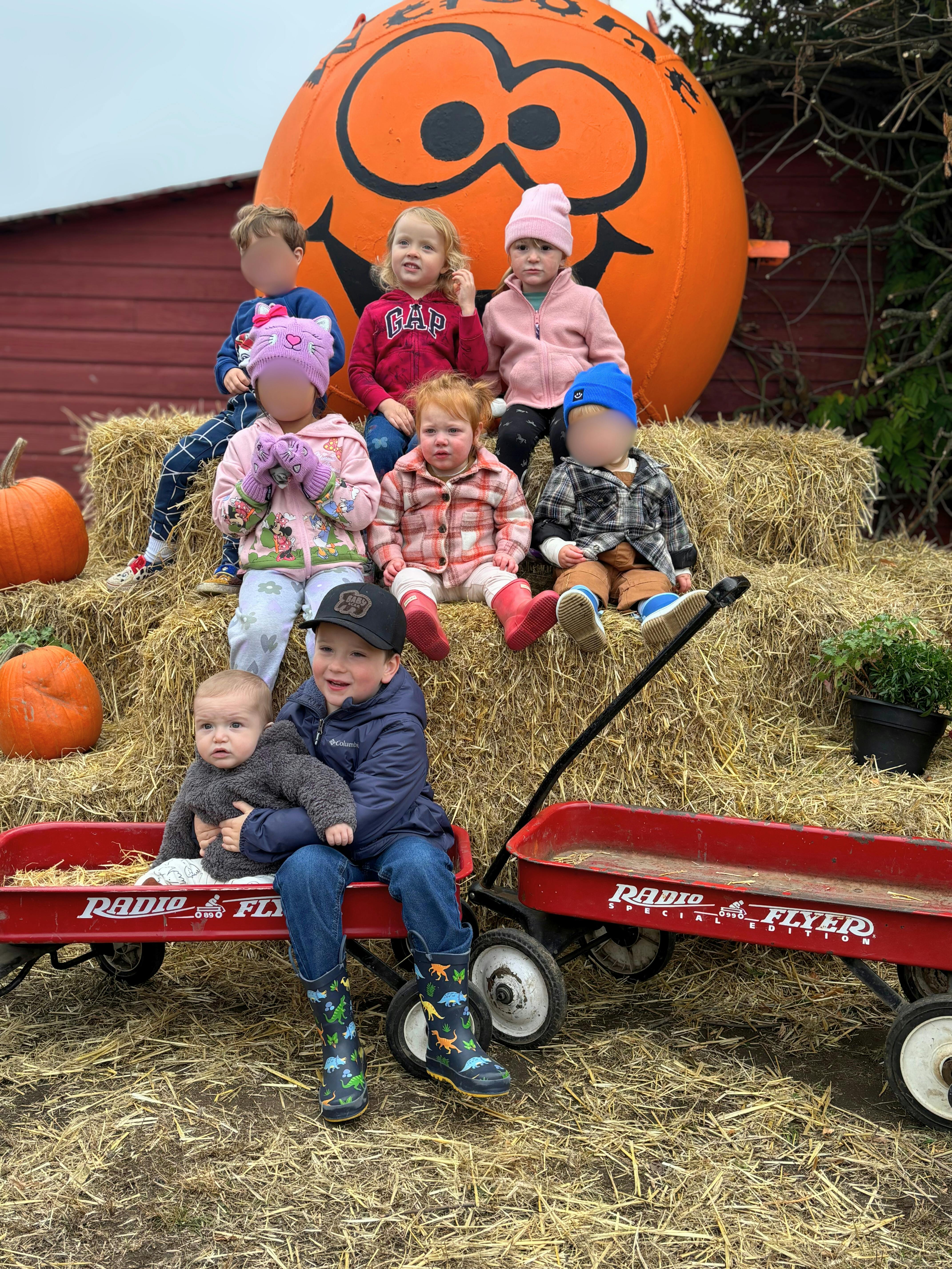 Children sitting on hay bales and in red wagons with a large pumpkin decoration