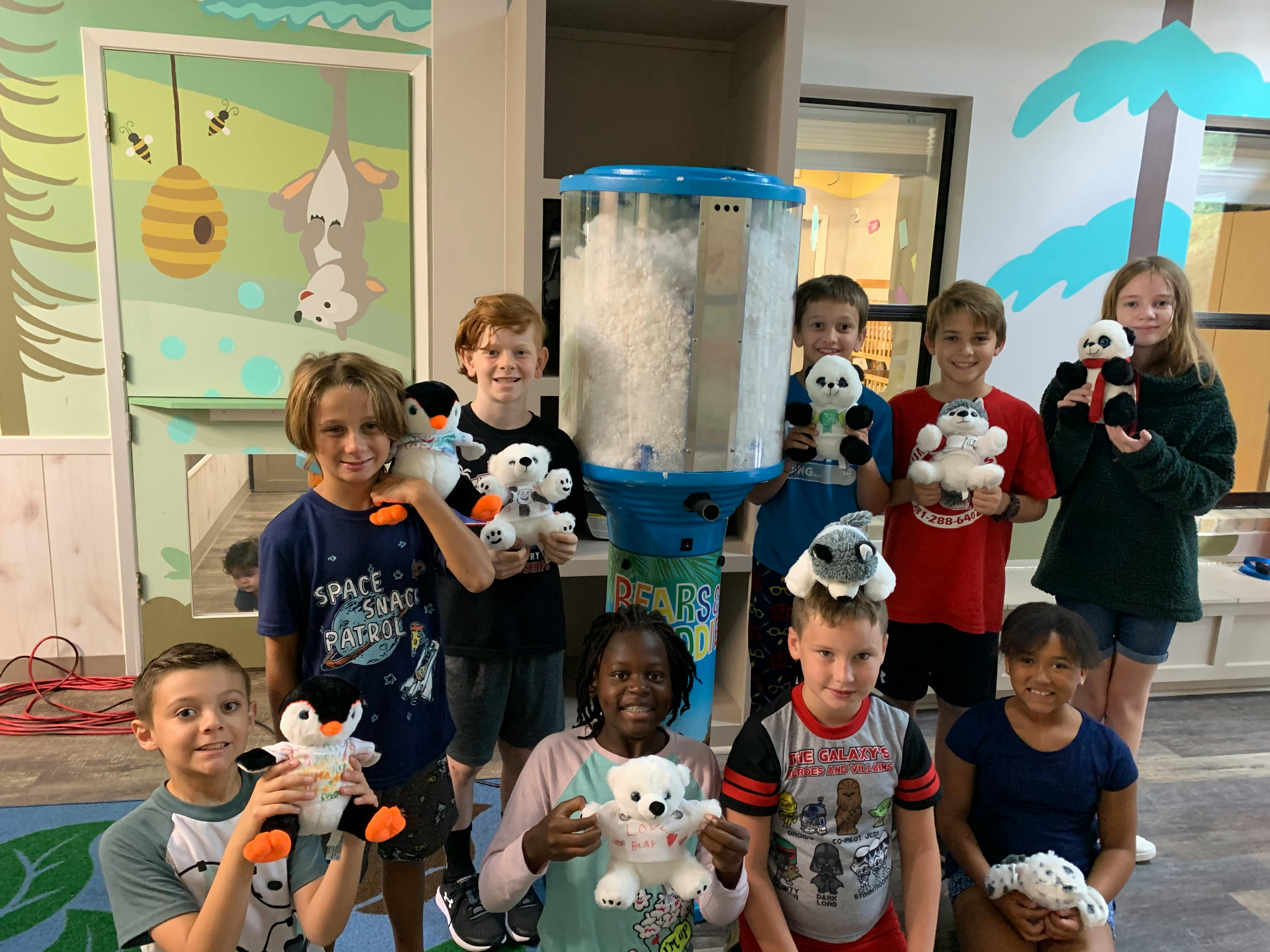 Group of children holding stuffed animals around a machine