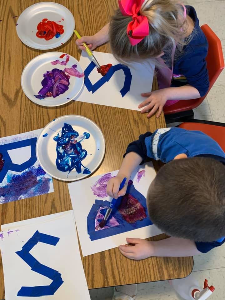 Two children painting letters on paper at a table