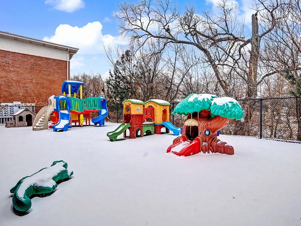 Snow-covered playground with slides, playhouses, and a tree-shaped climbing structure