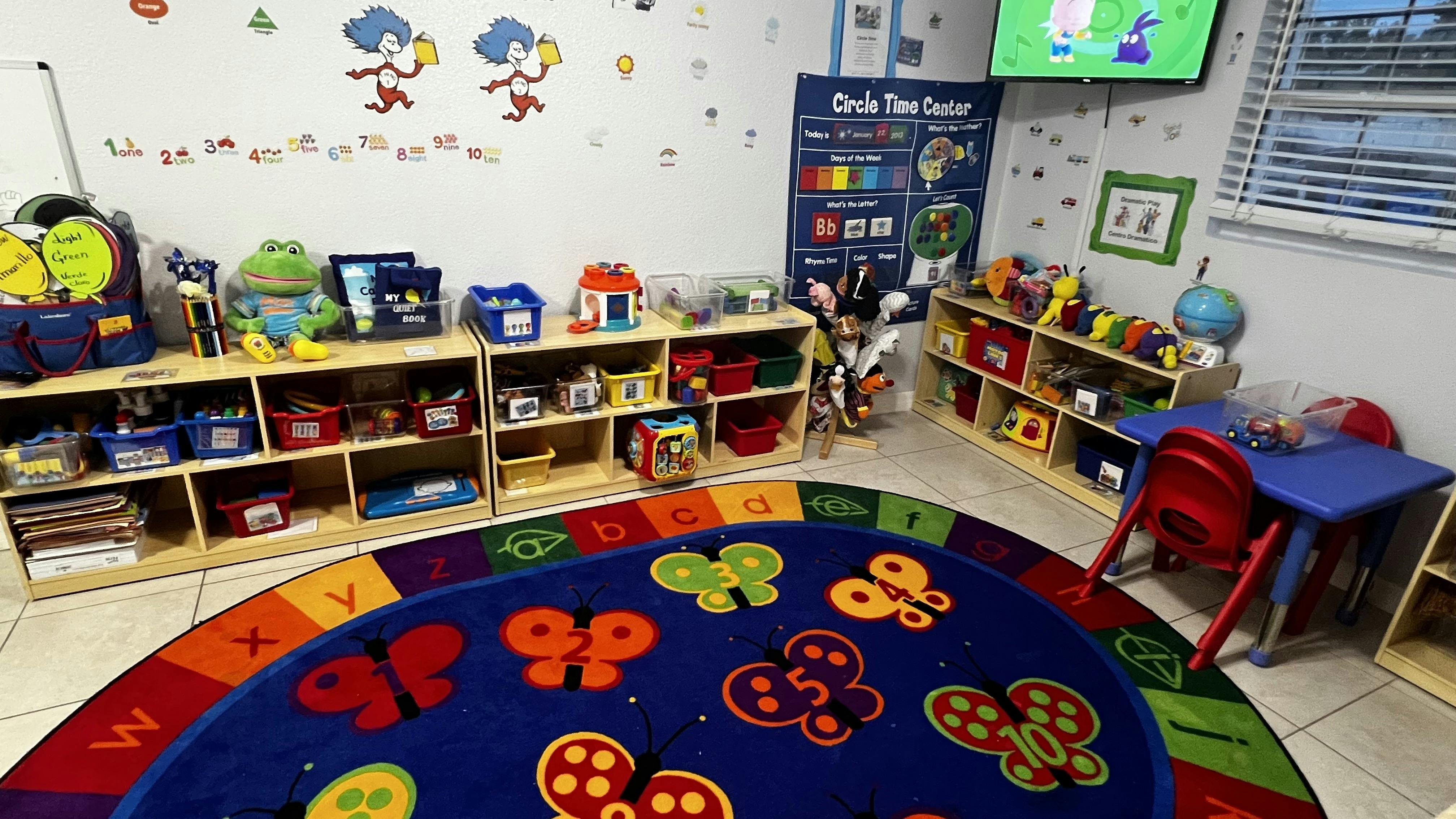 Classroom interior featuring shelves with toys and an alphabet rug