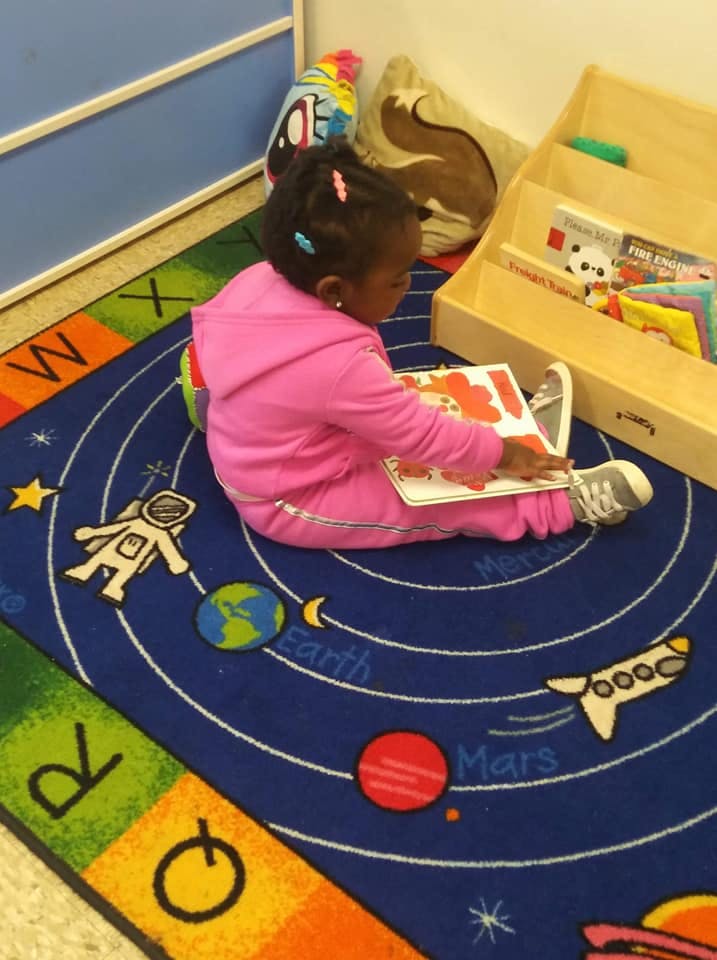 Child sitting on a solar system rug reading a book