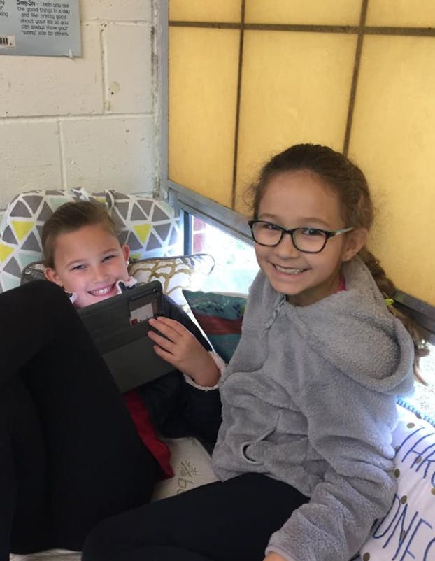 Two children sitting together, one holding a tablet