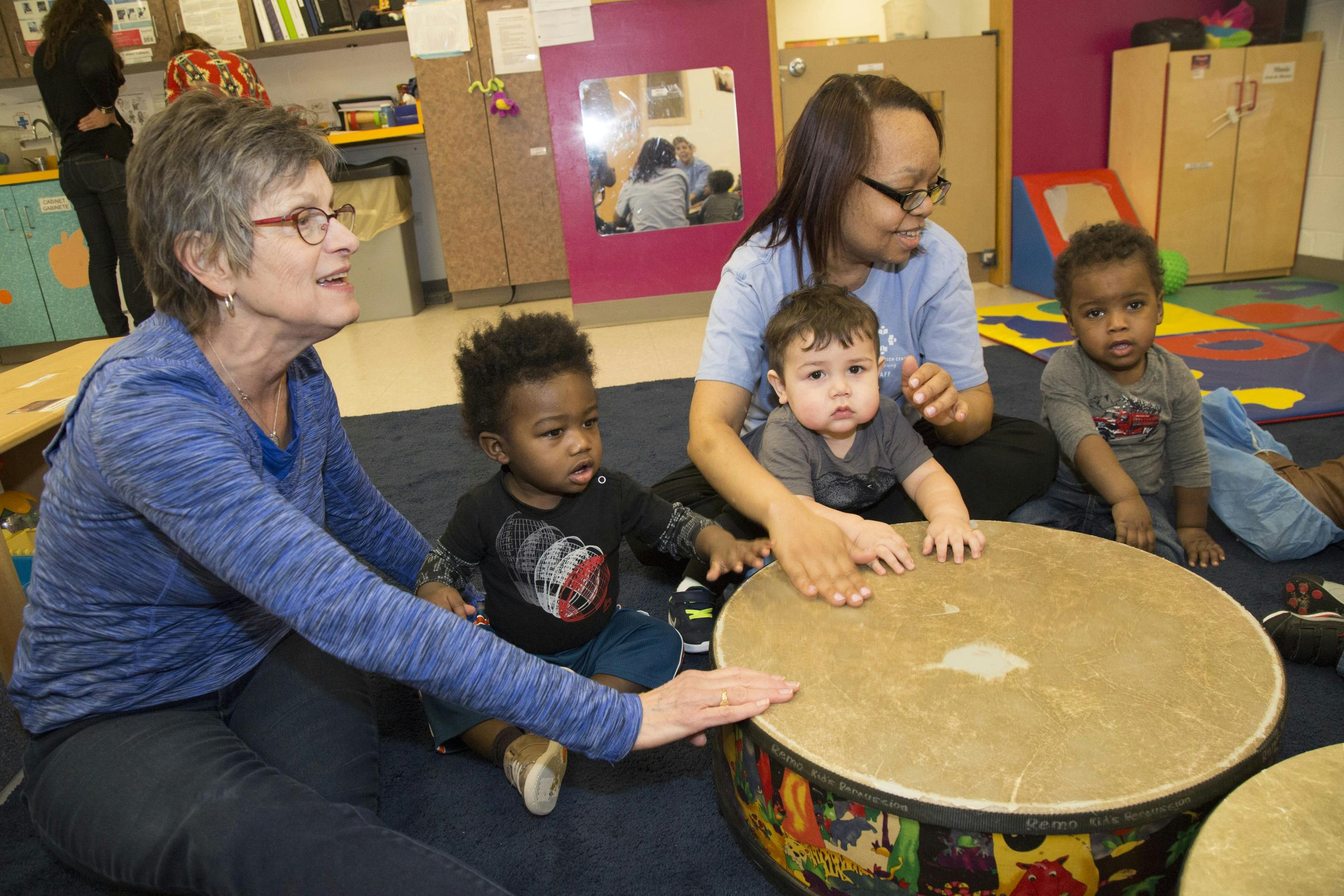 Two people and three children playing drums in a classroom