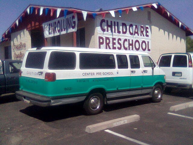 White and green van parked in front of a building with "CHILD CARE PRESCHOOL" sign