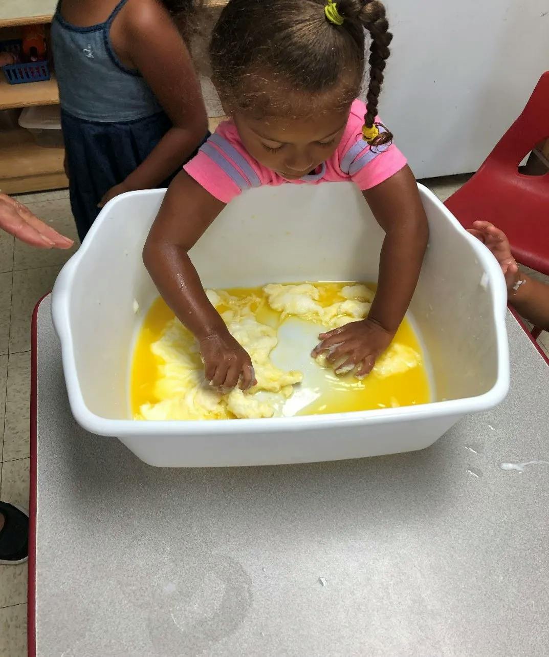 Child with hands in a white bin with yellow liquid and white solids
