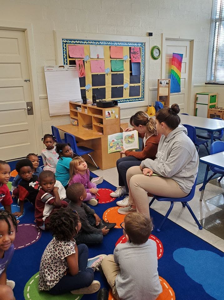 Two adults reading a book to a group of children in a classroom
