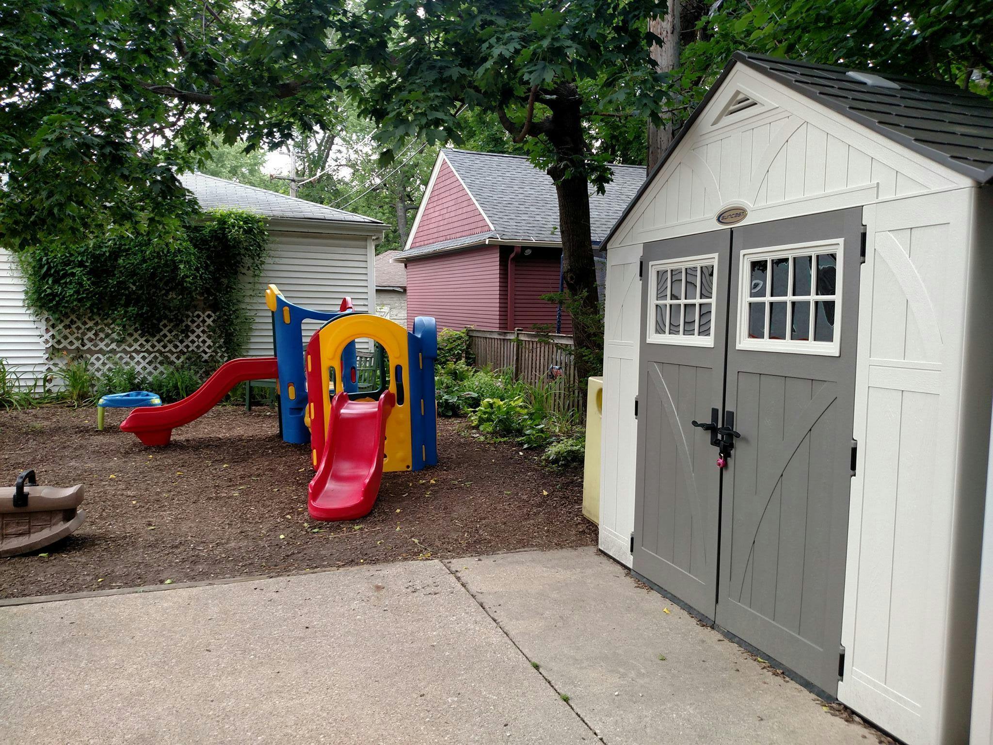 White shed with gray doors next to a colorful playground set