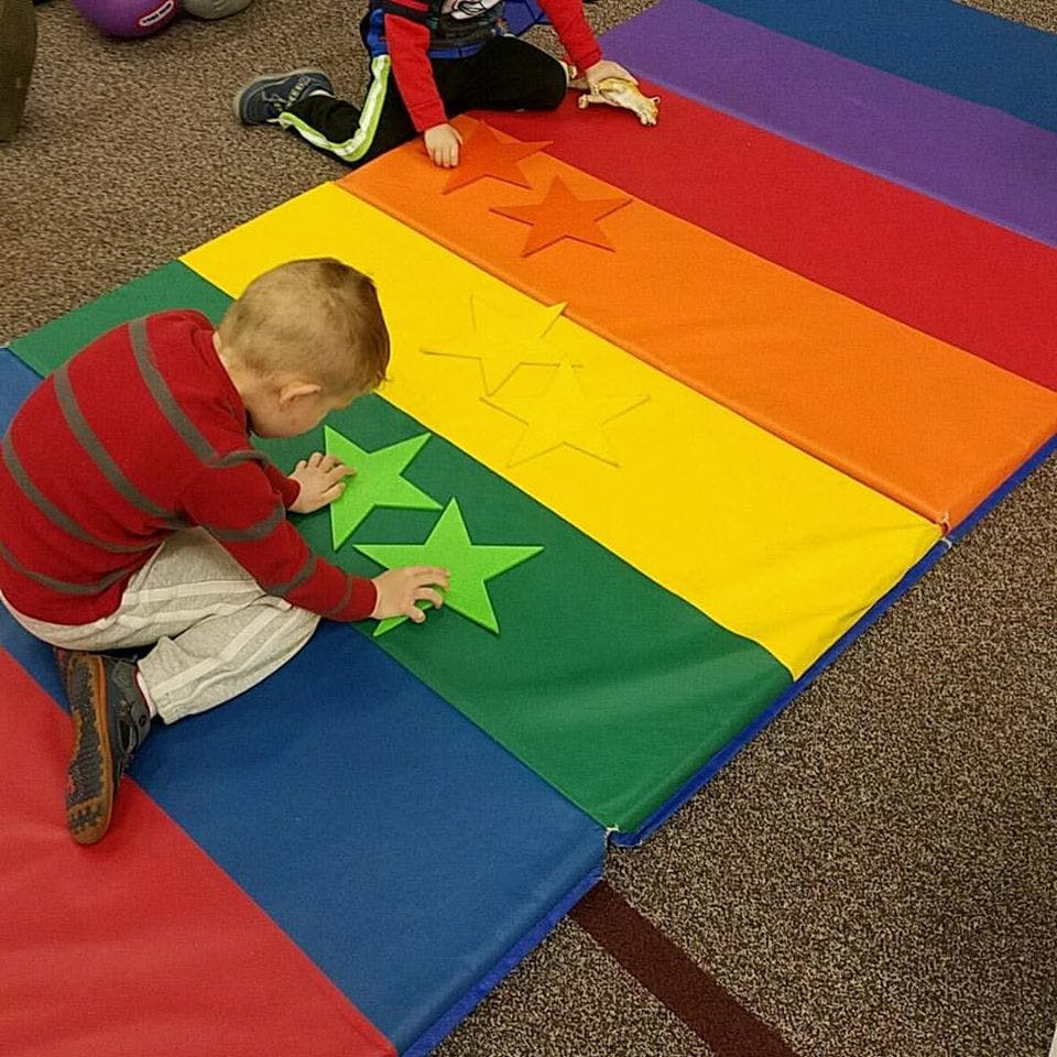 Child playing with green stars on a rainbow-colored mat