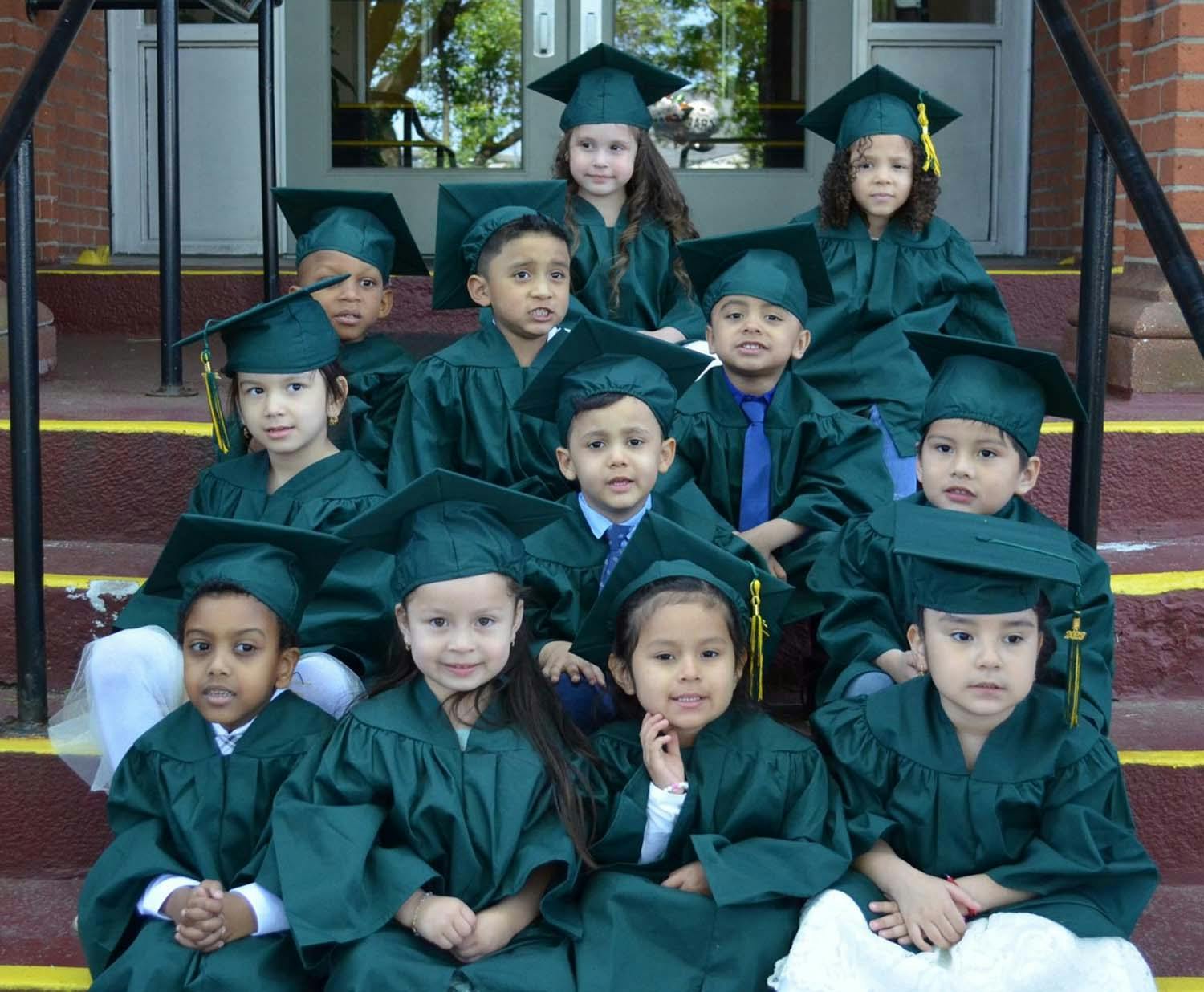 Group of children wearing green graduation caps and gowns sitting on steps