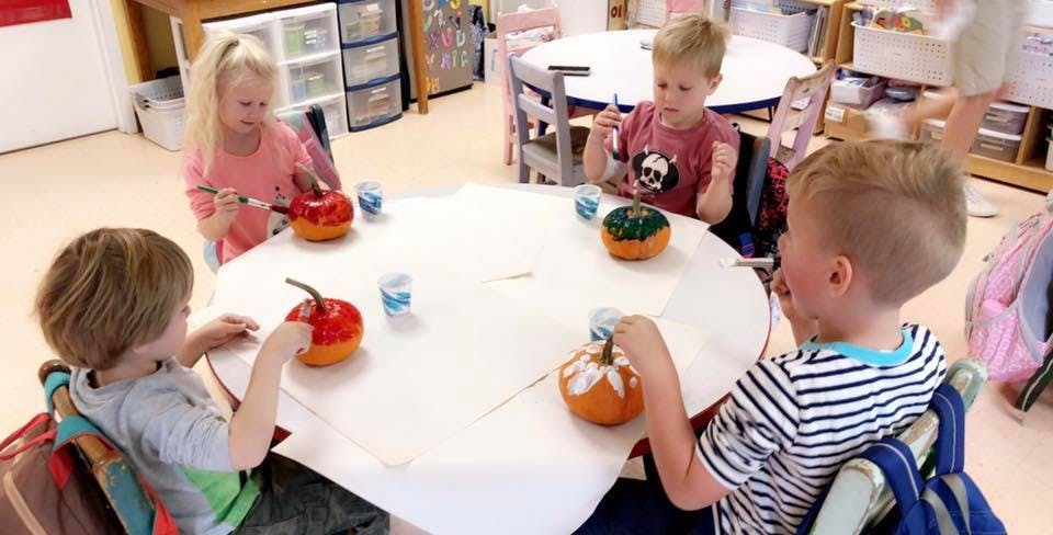 Children painting pumpkins at a table in a classroom