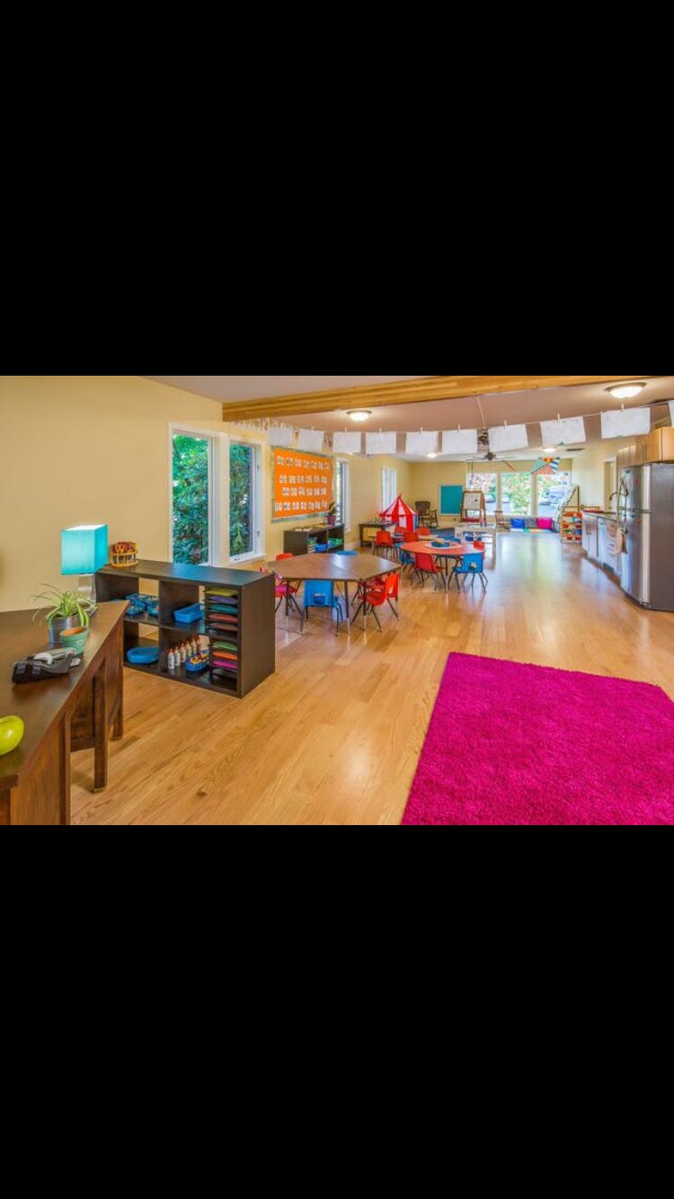 Classroom with small tables and chairs, shelves, and a pink rug