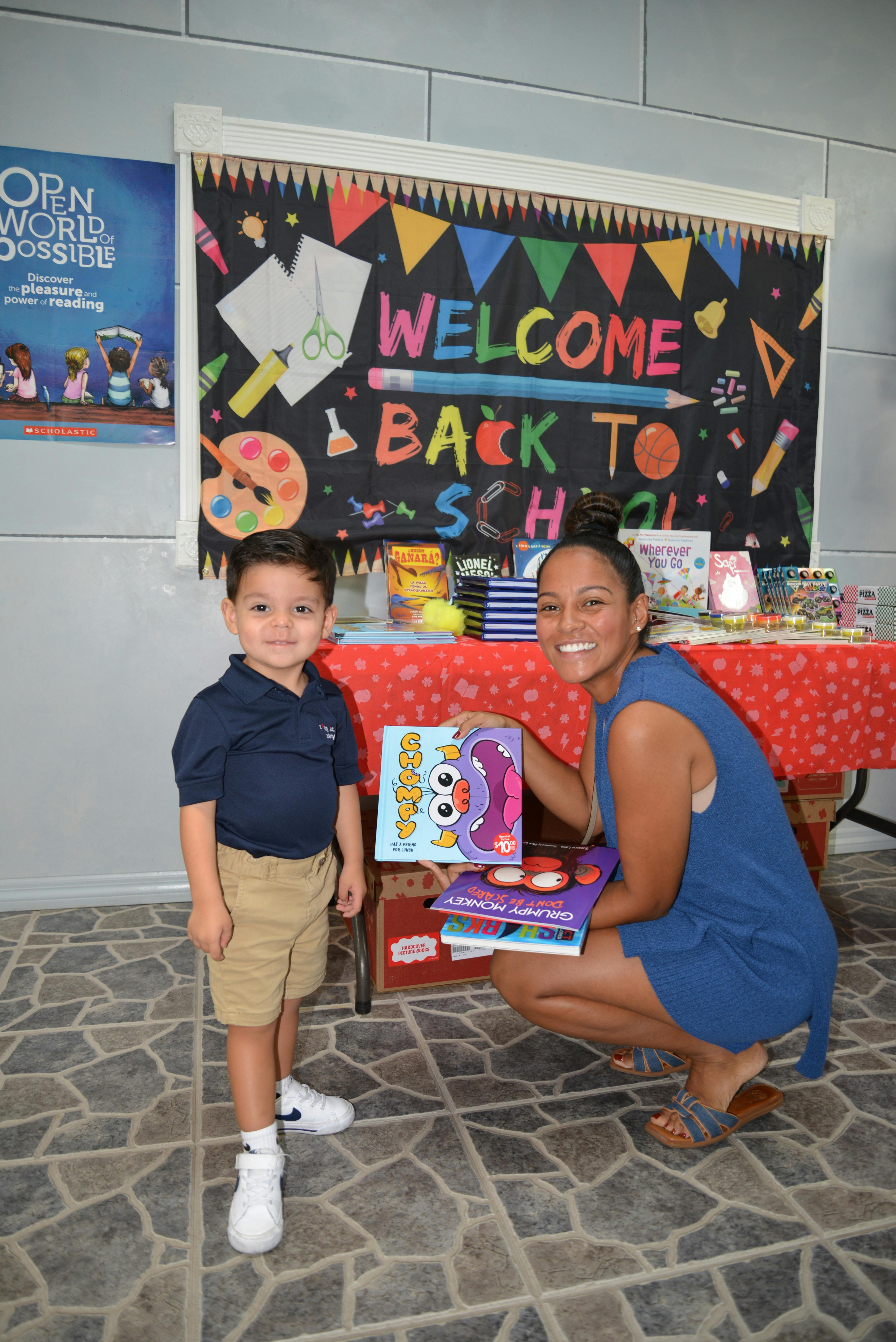 Adult and child with books in front of a "Welcome Back to School" sign