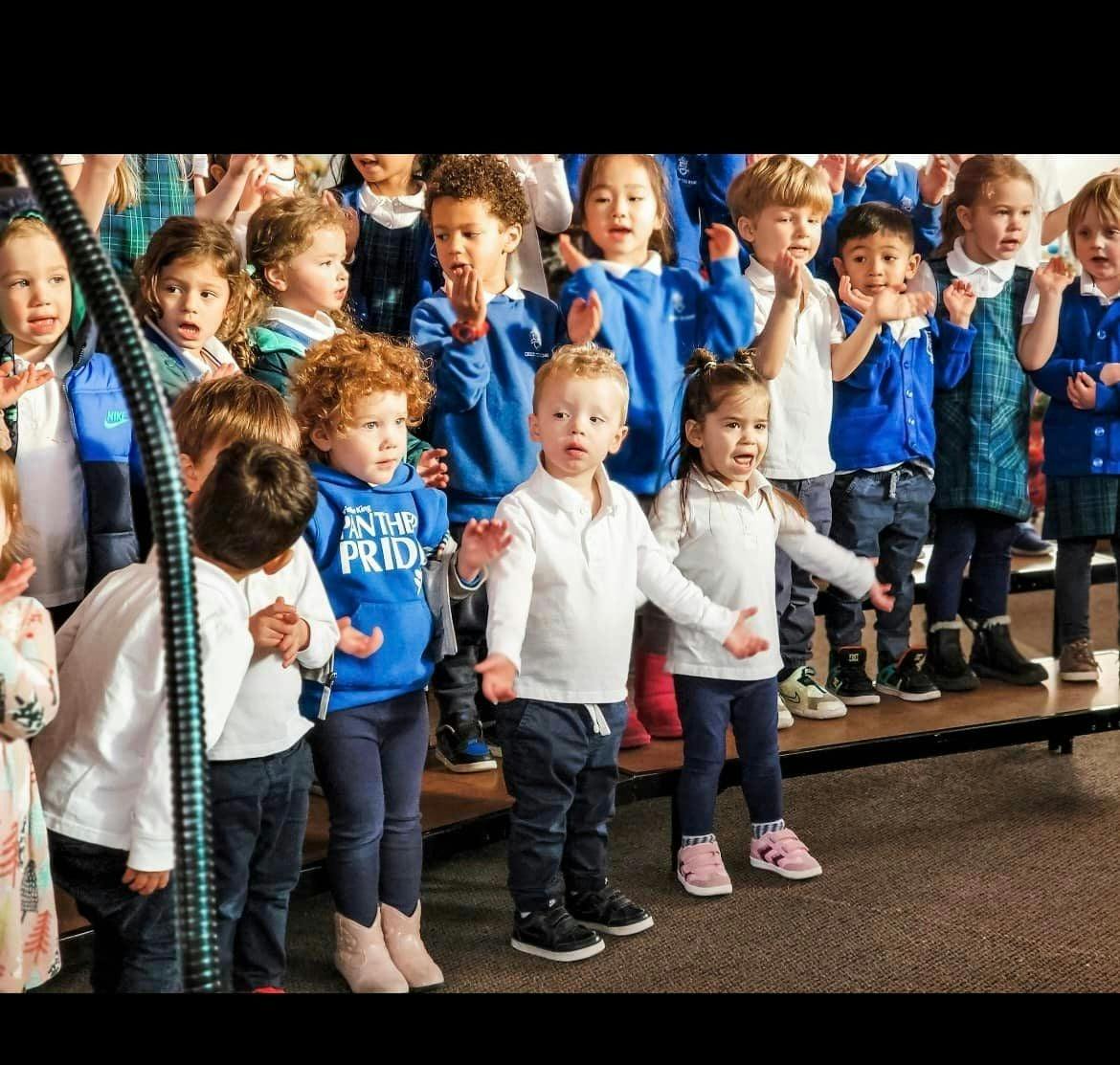 Group of children standing on risers, some with hands raised