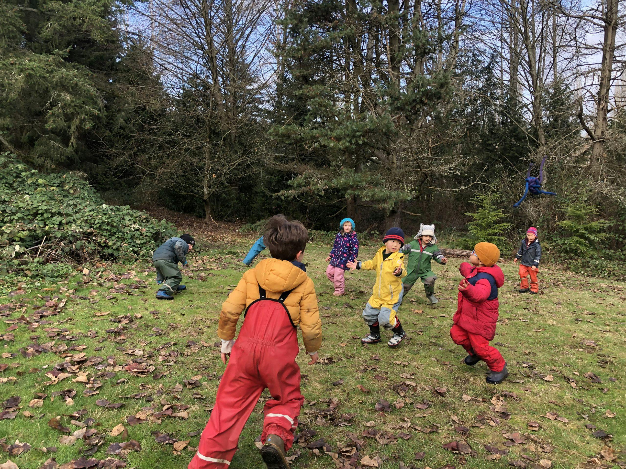 Group of children playing outdoors in a grassy area with trees