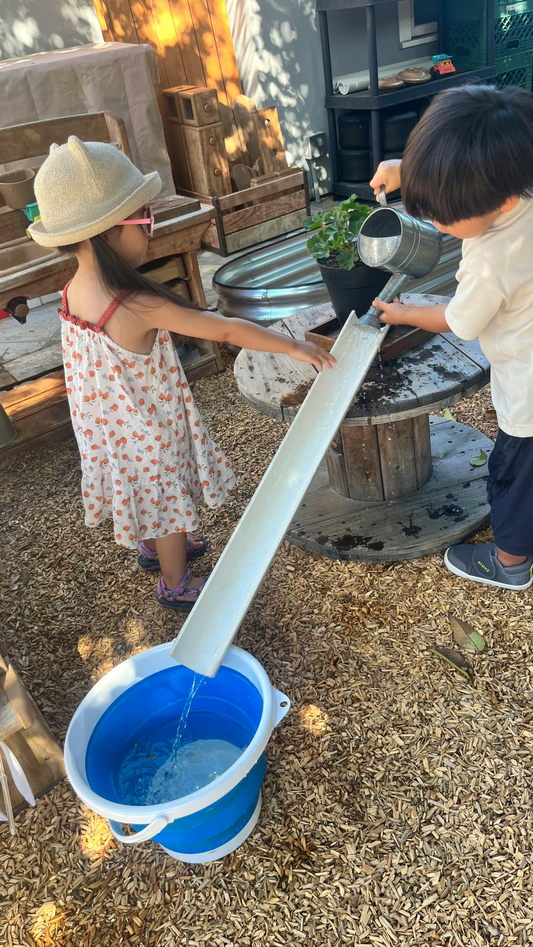 Two children pouring water down a chute into a blue bucket