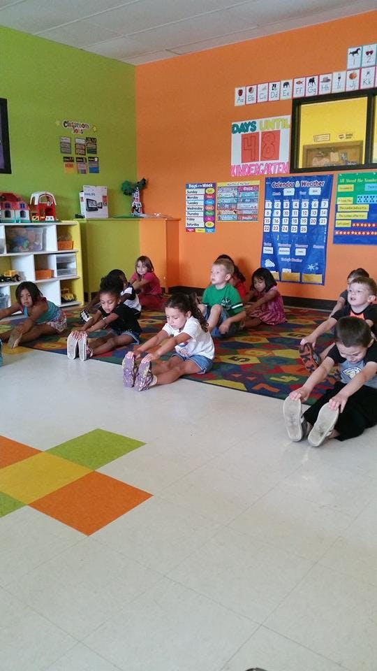 Children sitting on a rug stretching in a classroom