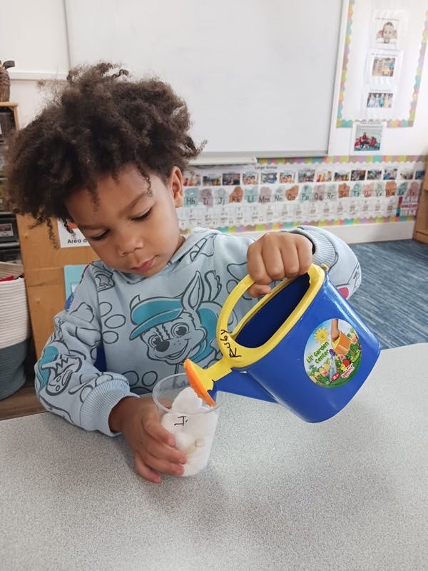Child pouring from a small watering can into a cup