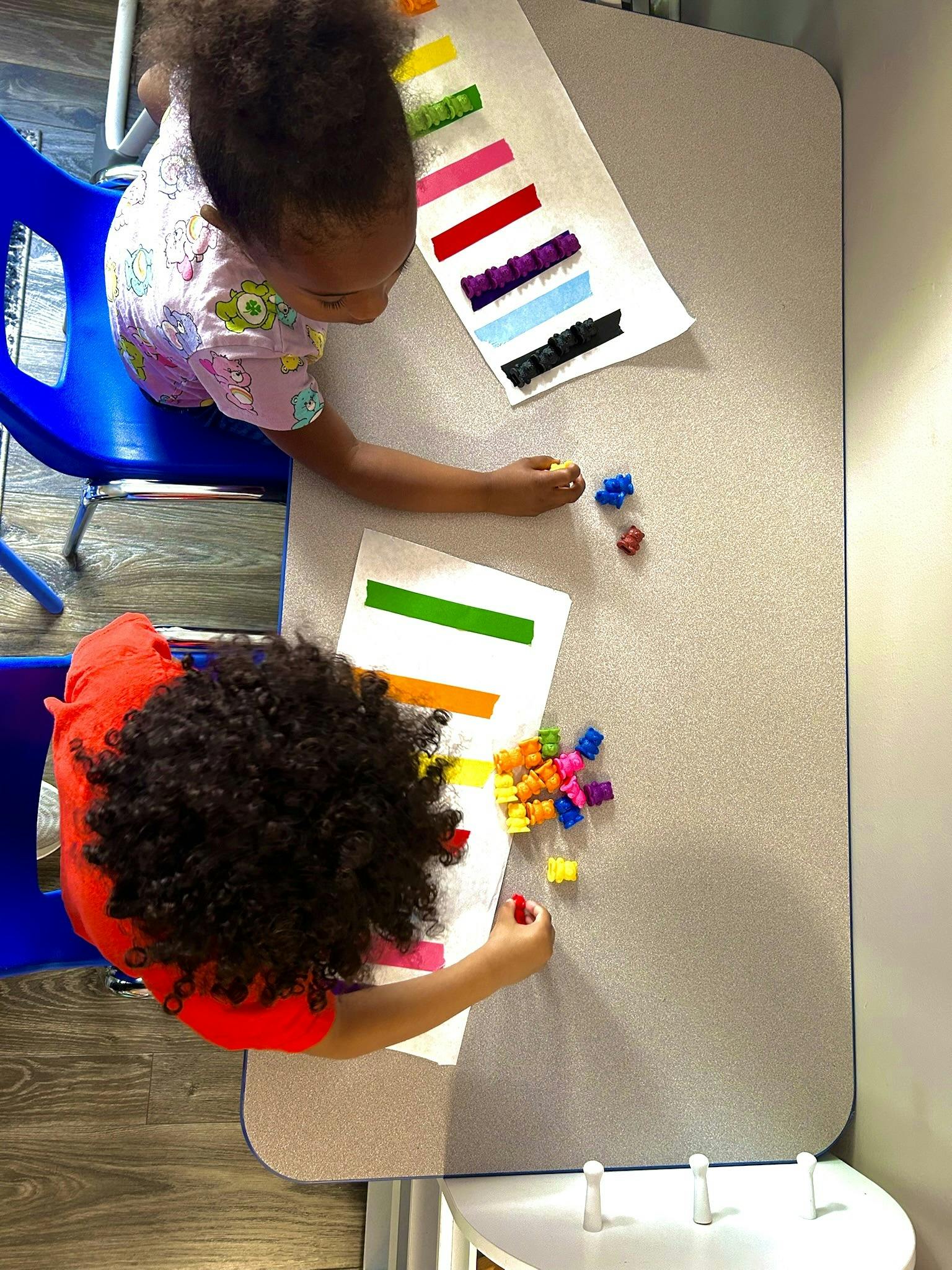 Two children at a table with colorful strips of paper and small objects
