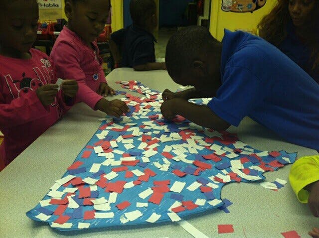Children decorating a large blue cutout with red and white paper pieces