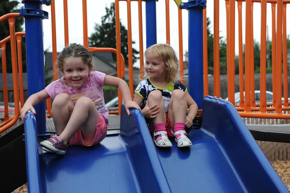 Two children sitting on a blue slide on a playground