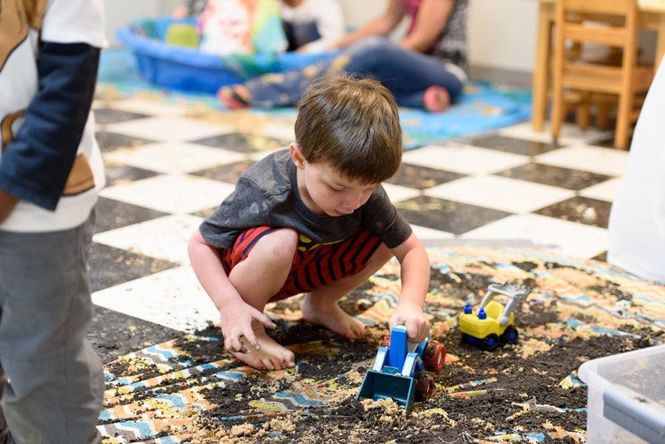Child playing with toy truck in sand and sand on sand