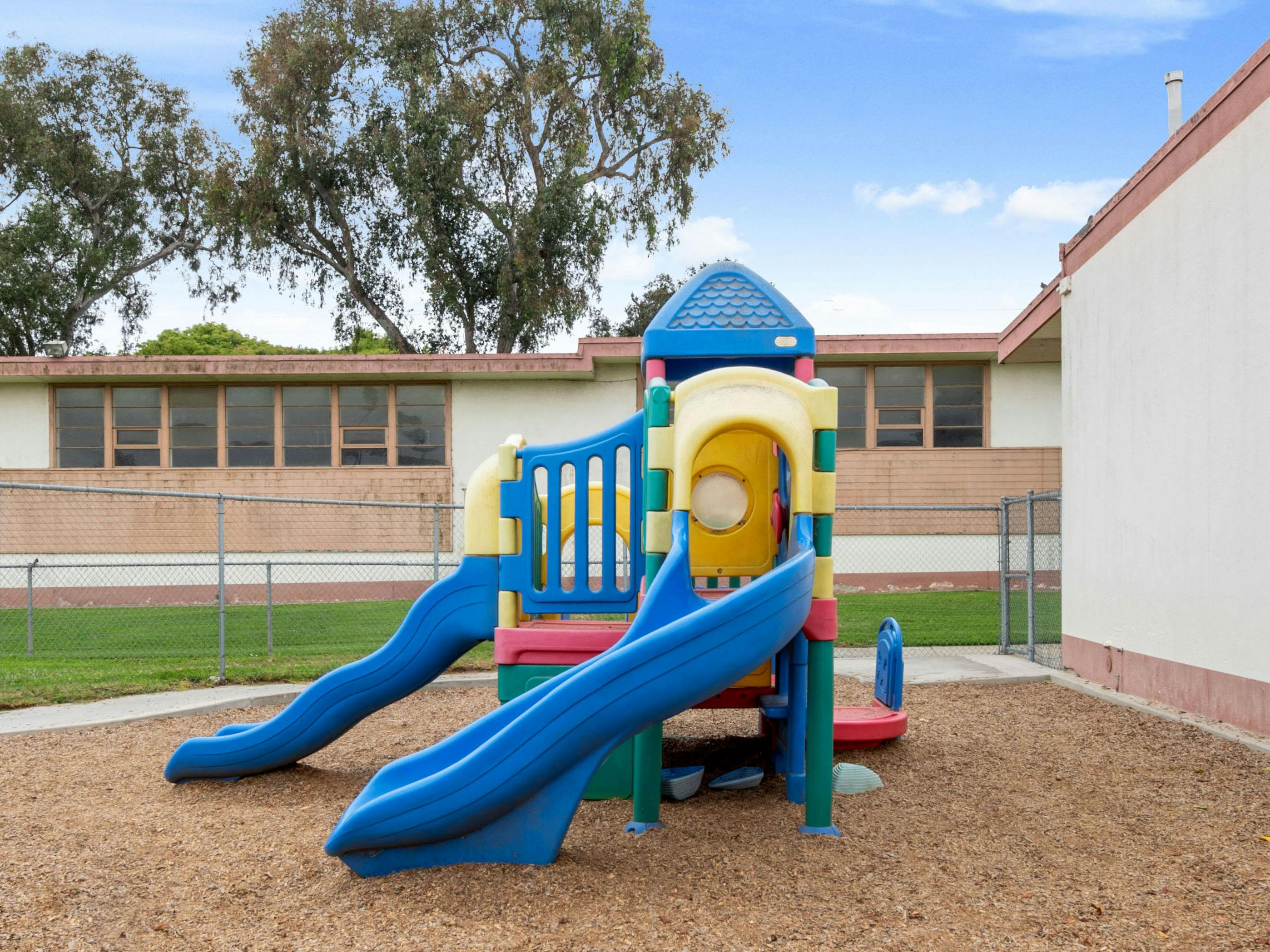 Colorful playground structure with two blue slides and wood chips on the ground