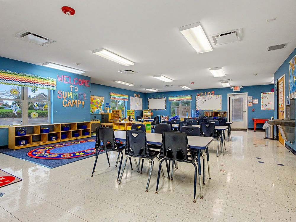 Classroom with small tables and chairs, blue walls, and a colorful rug