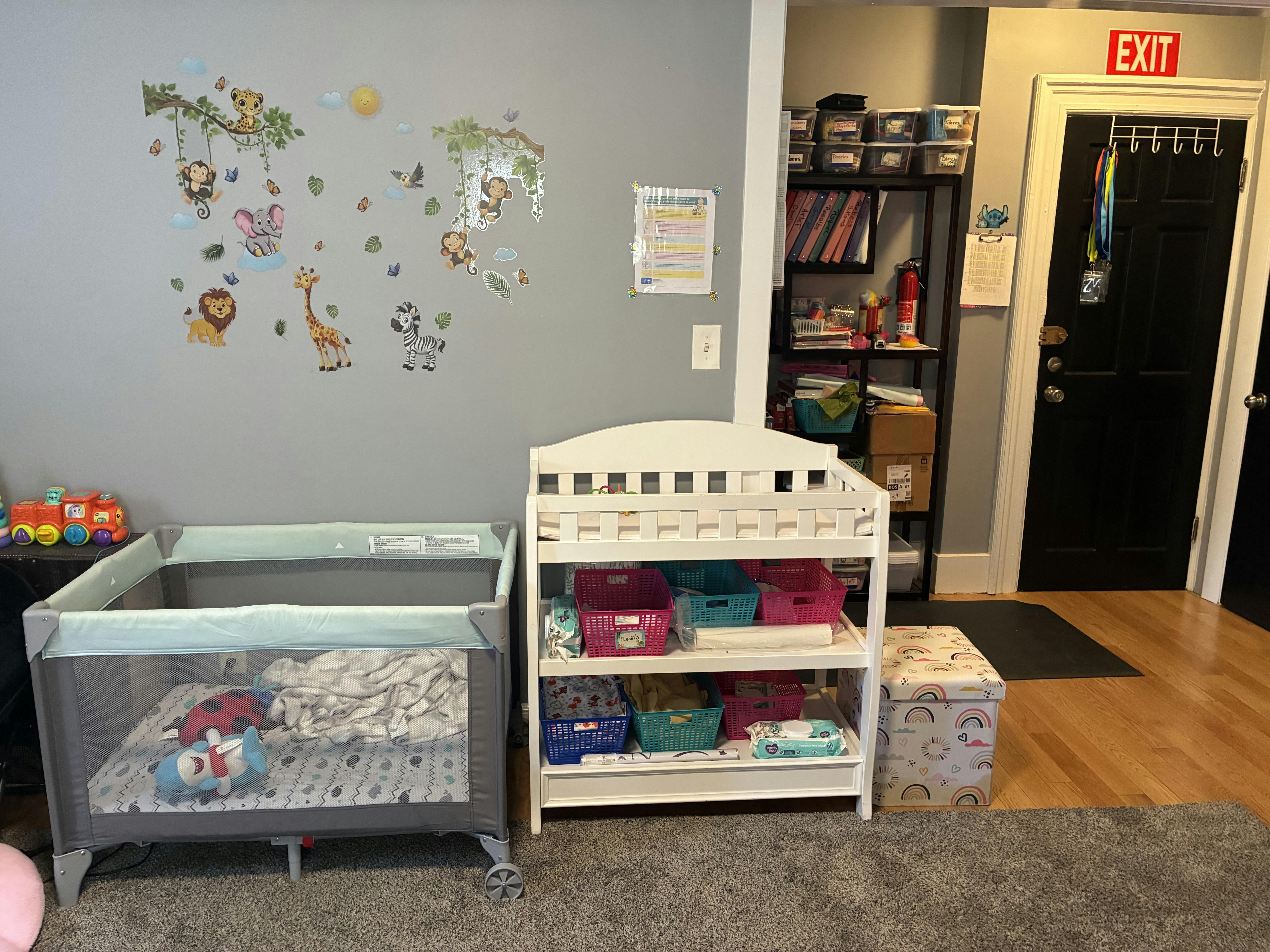 Playpen and changing table with animal decals on the wall in a childcare room