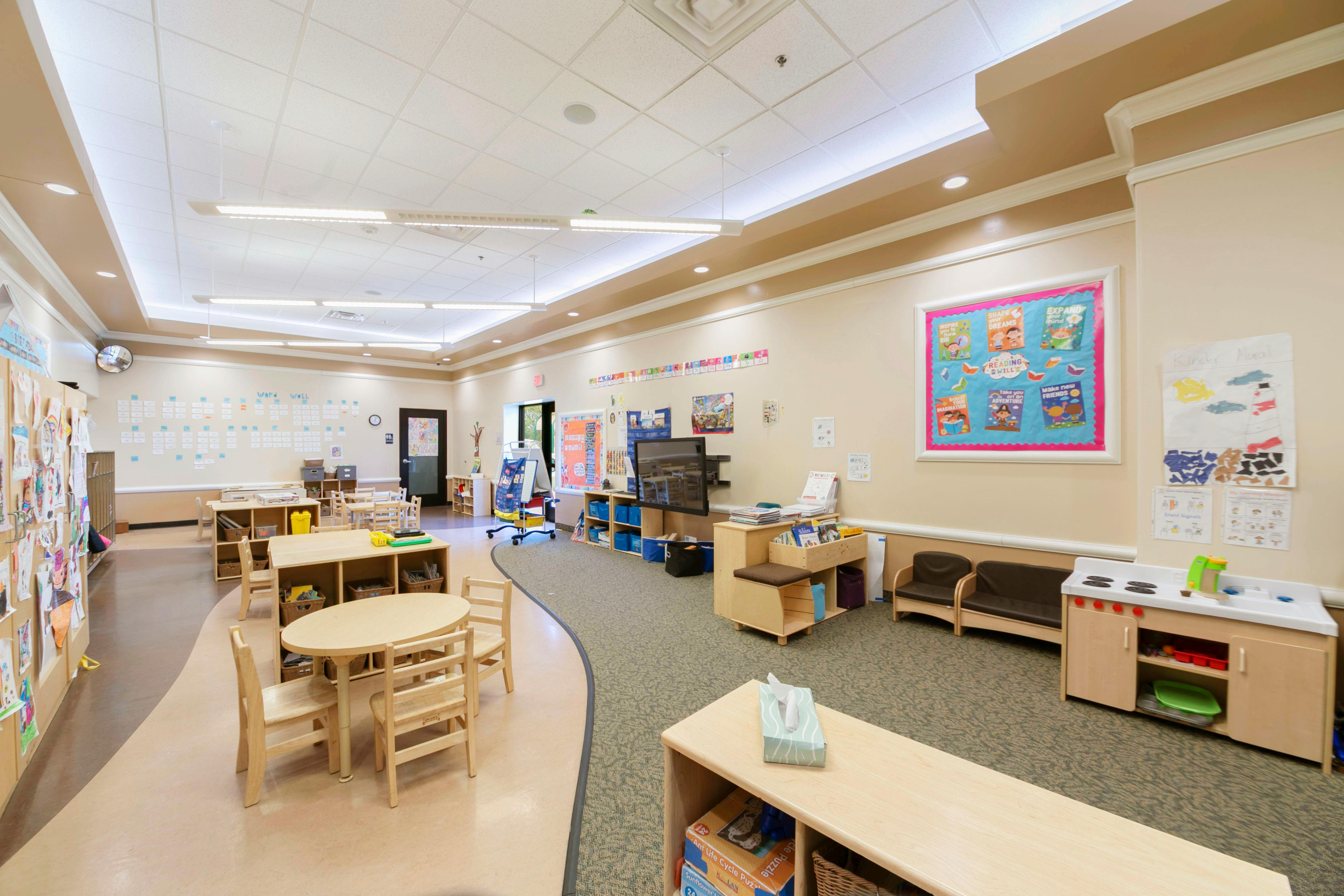 A classroom with small tables and chairs, shelves, and a play kitchen area