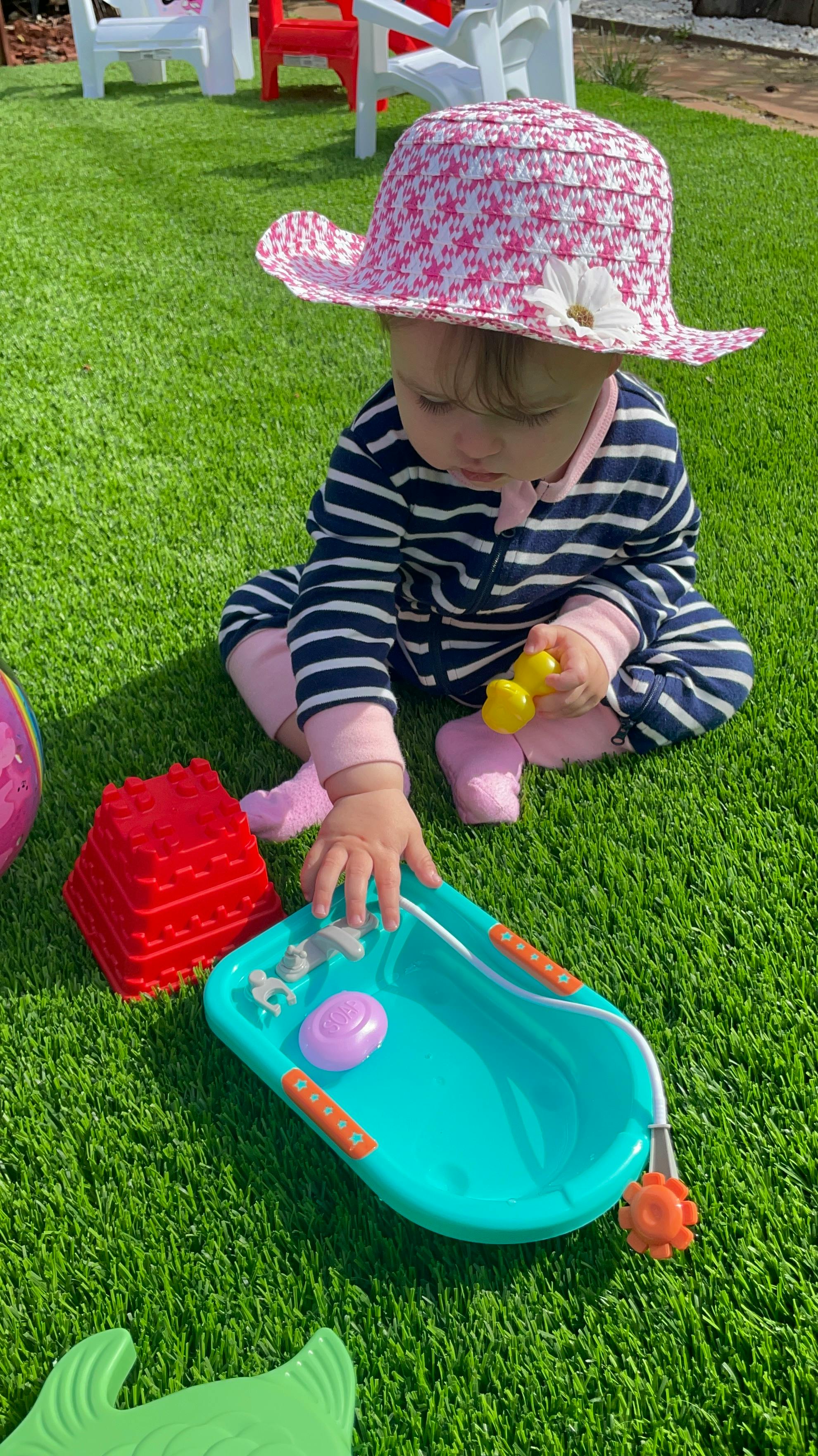 Child in a hat playing with toys on artificial grass