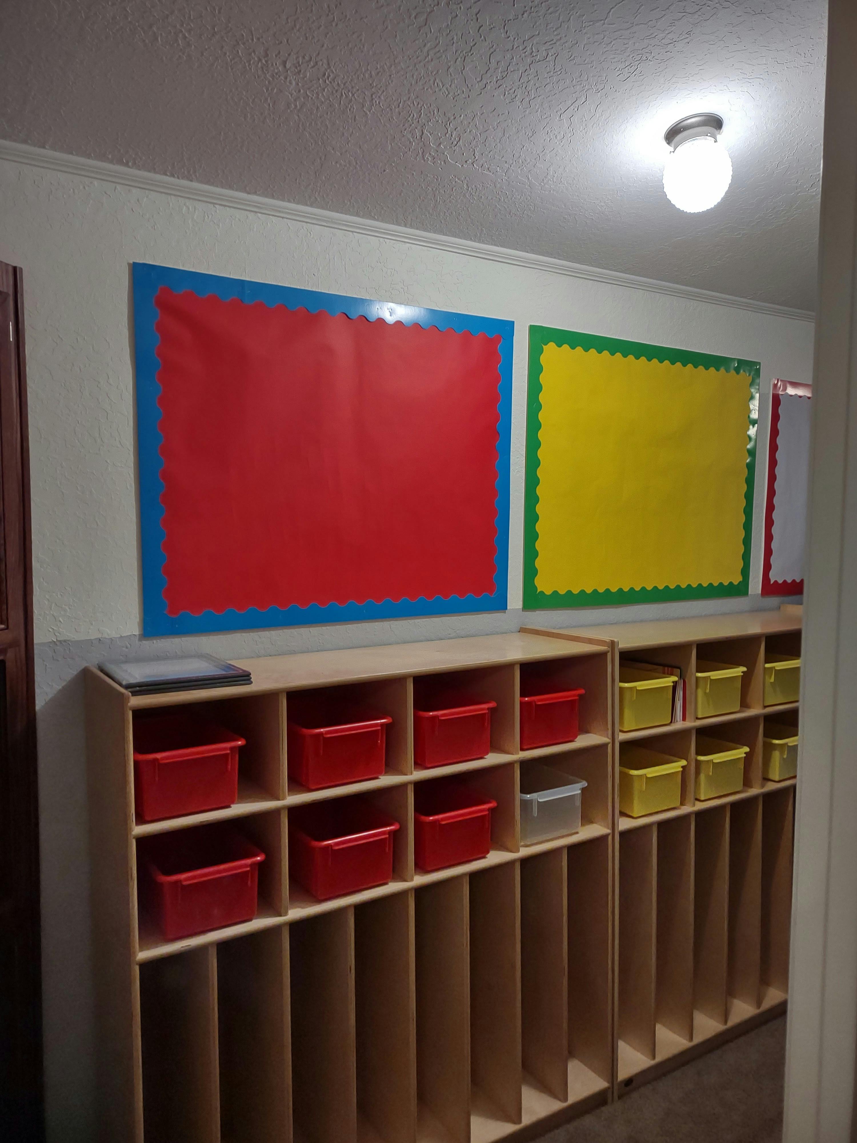 Classroom cubbies with red and yellow bins below bulletin boards