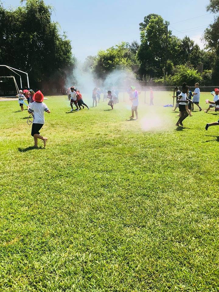 People running through colored smoke on a grassy field