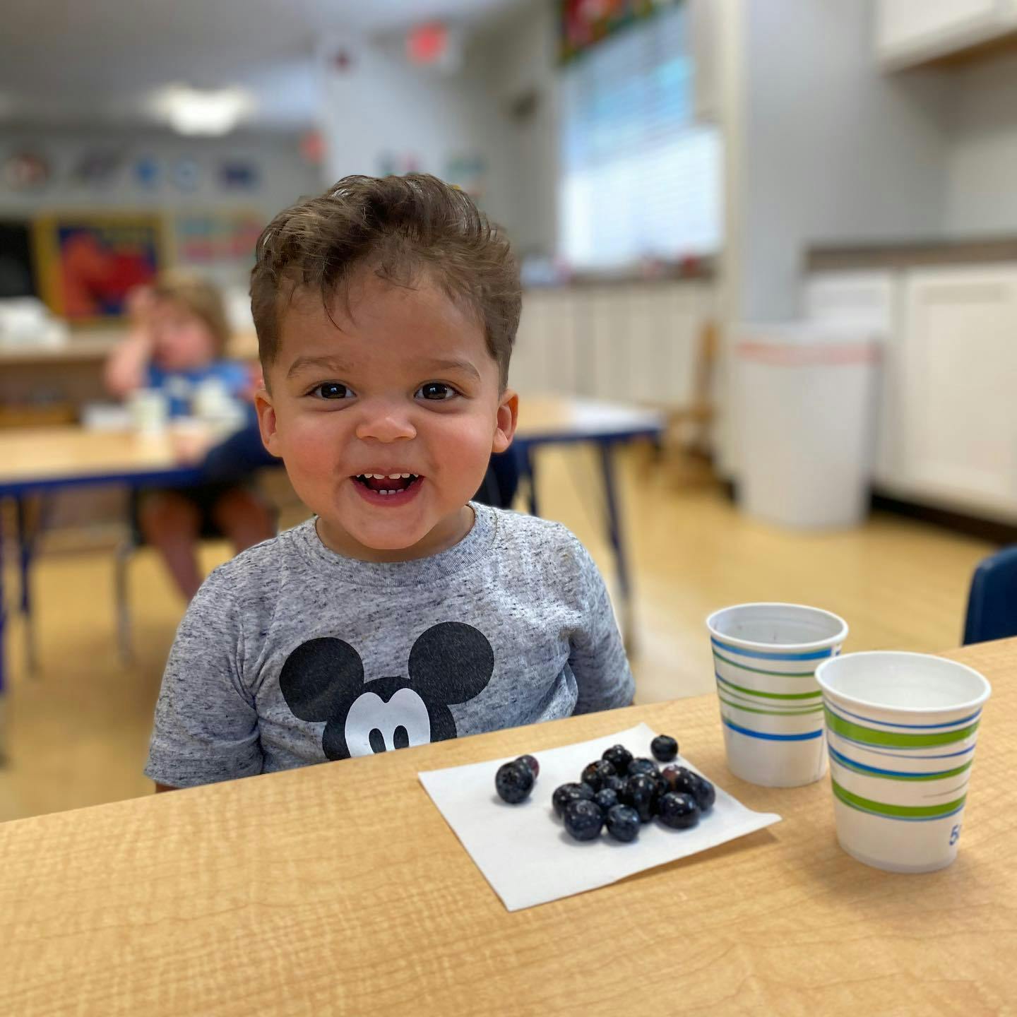 Child at a table with blueberries and cups in a classroom