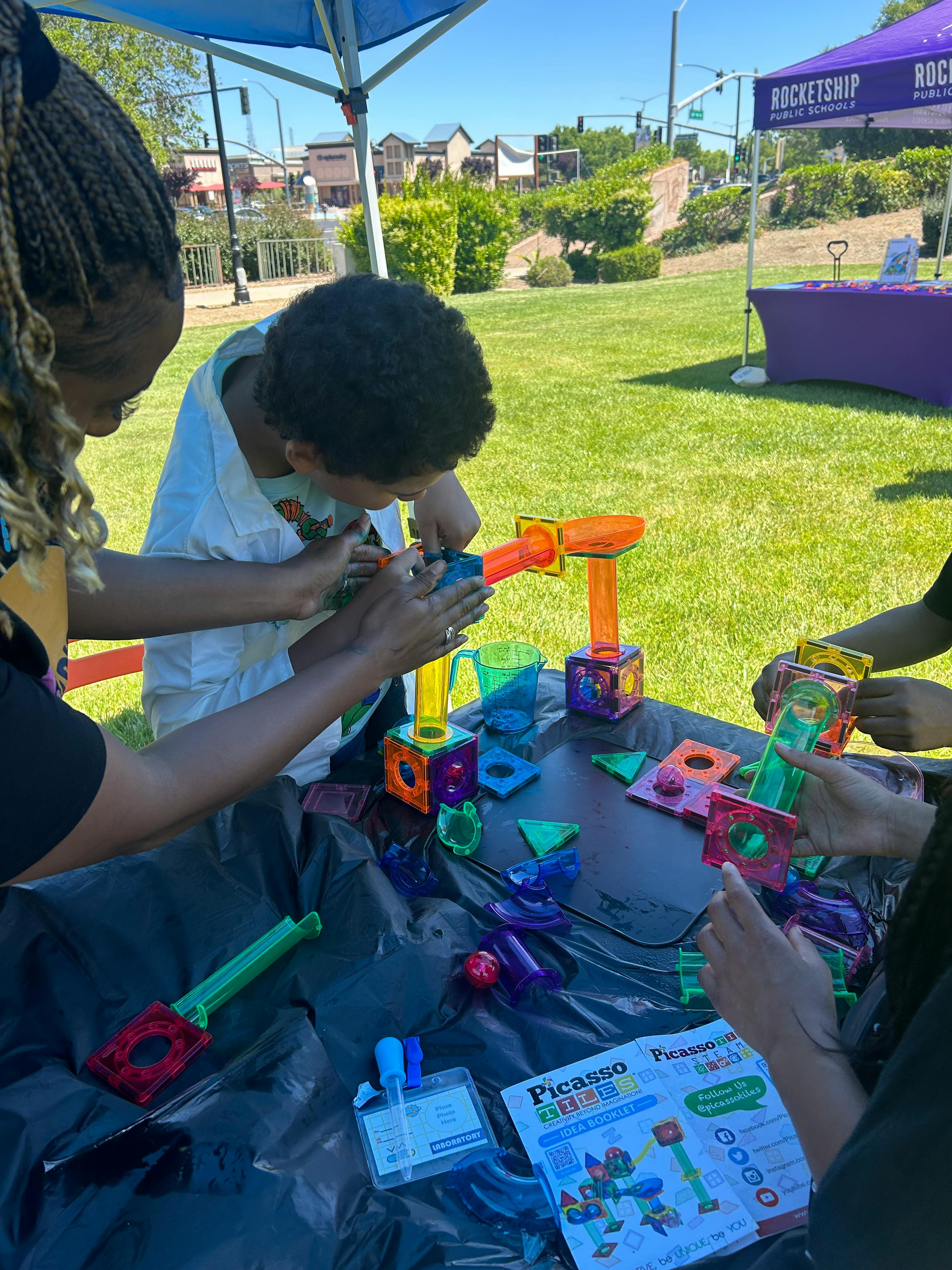 Adult and child building with colorful magnetic tiles at a table outdoors
