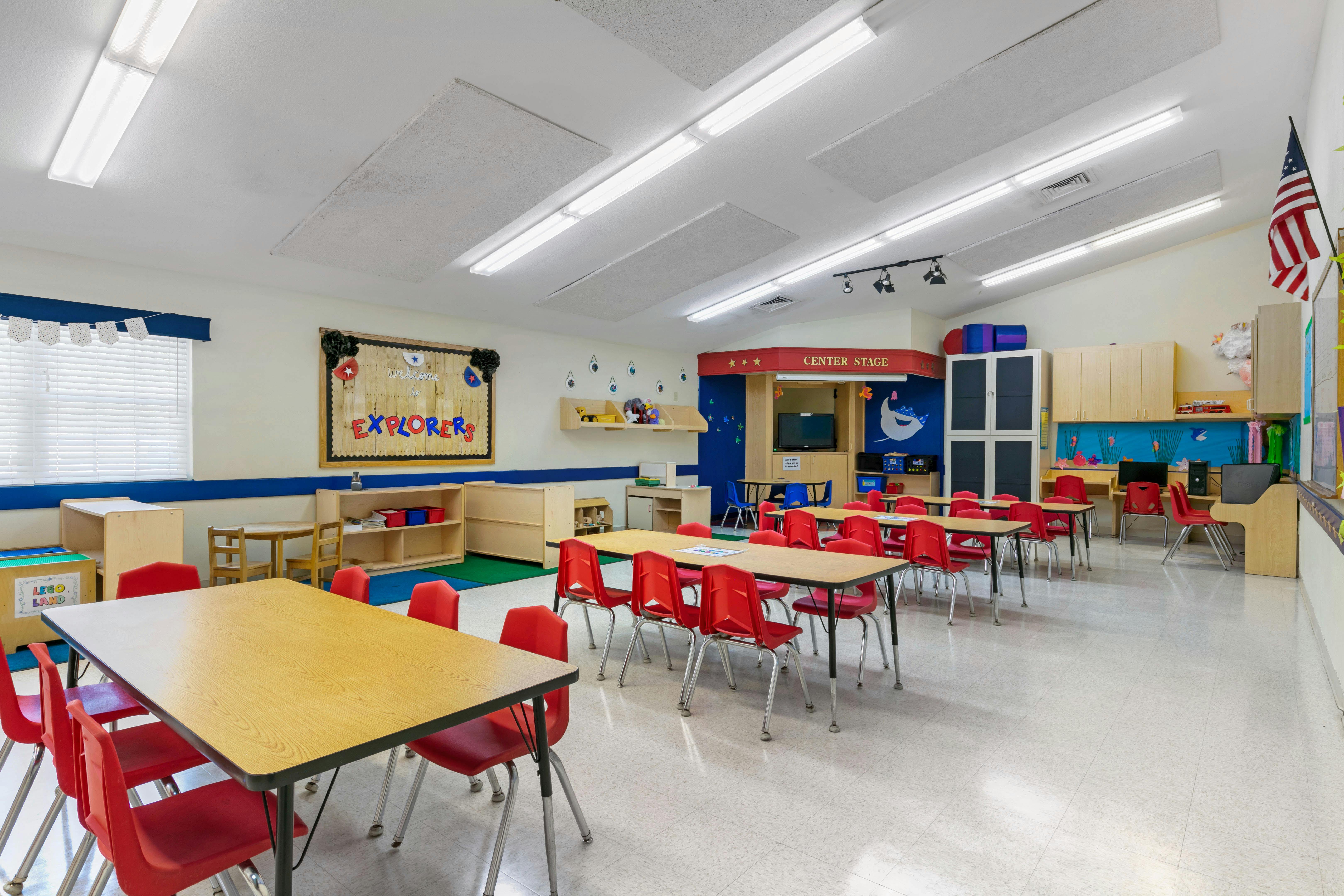 Classroom with small tables and red chairs, a "Center Stage" area, and a bulletin board