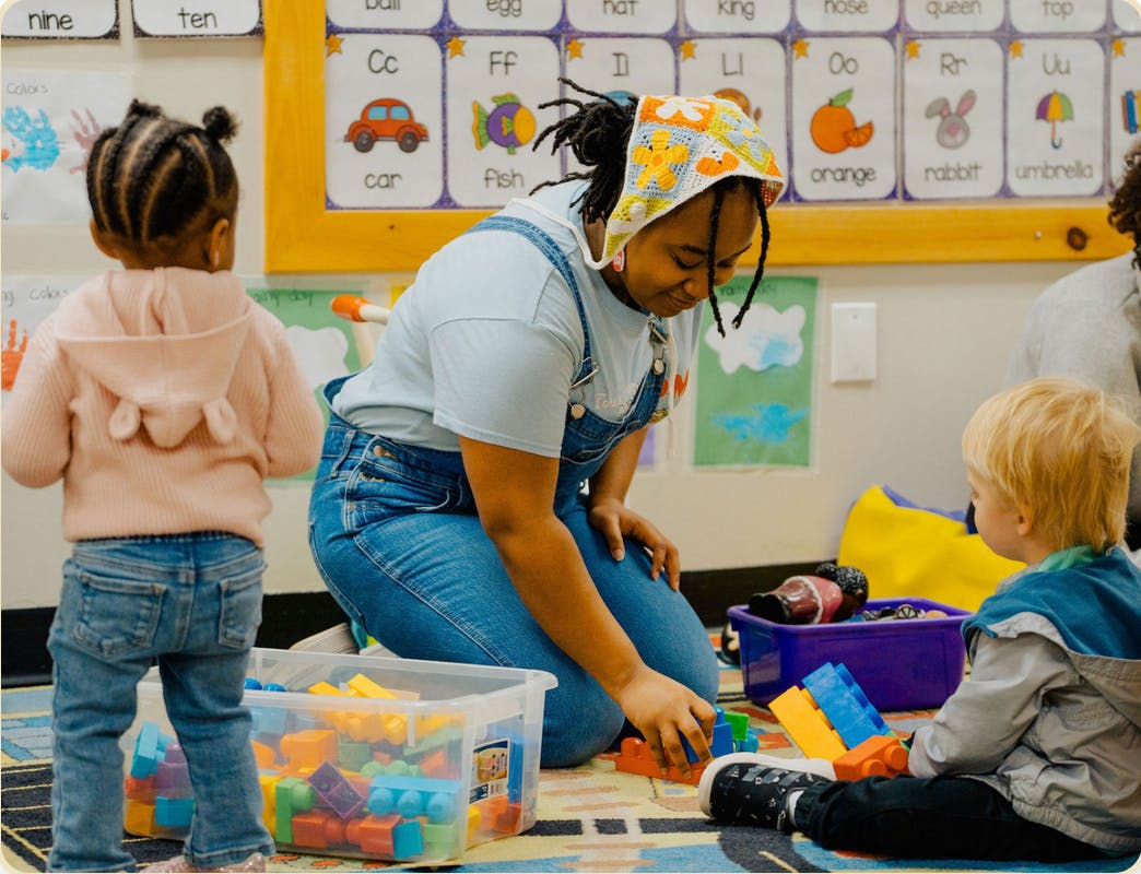 Person kneeling, playing with blocks with a child in a classroom