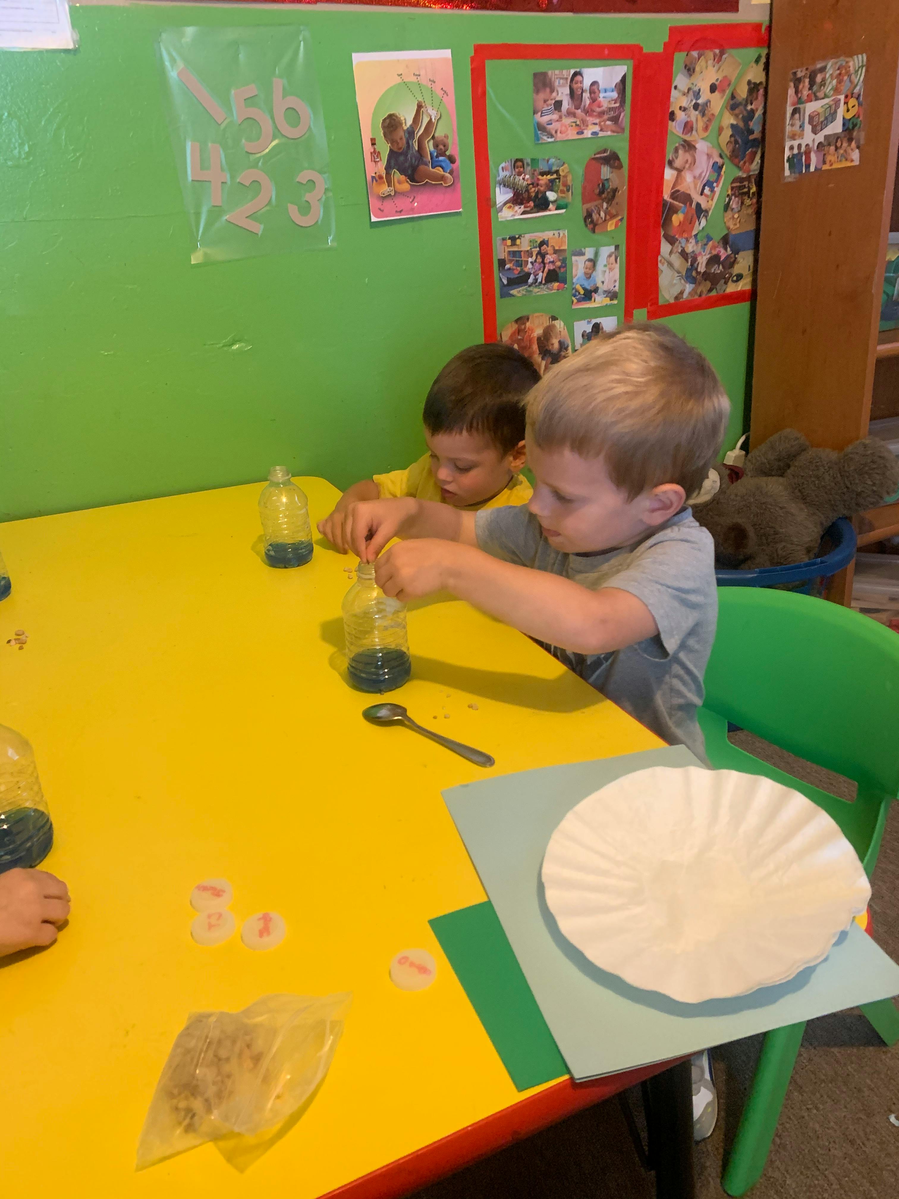Two children at a yellow table with bottles and spoons