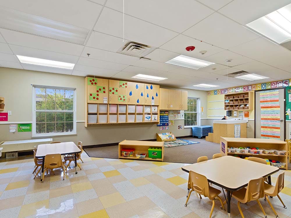 Empty classroom with small tables and chairs, storage cabinets, and a colorful floor