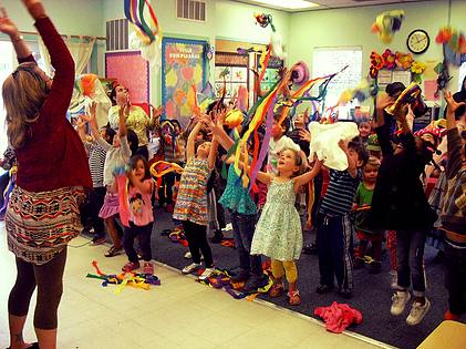 Adult and children with arms raised, holding colorful ribbons and white objects