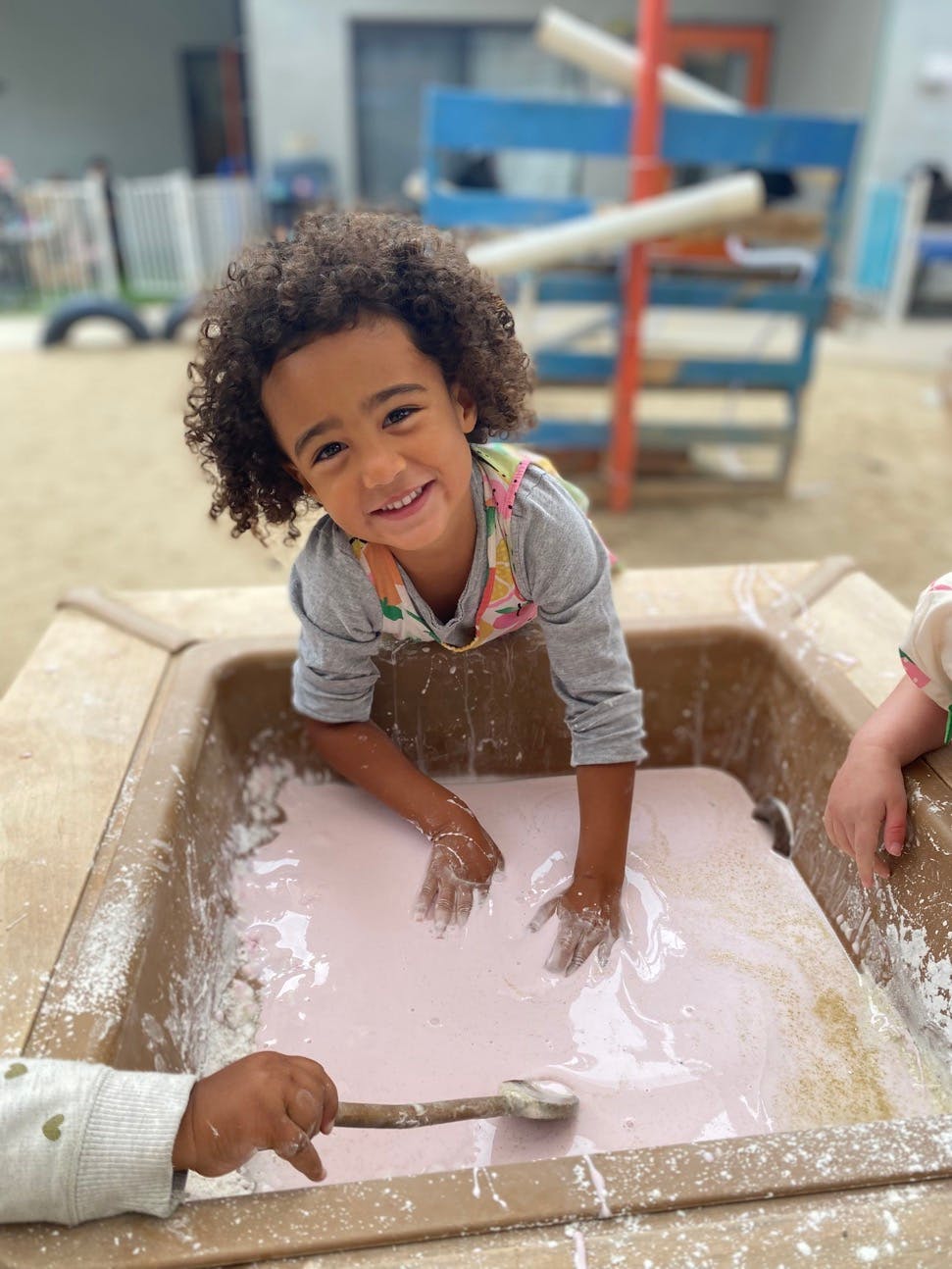 Child smiling while playing in a container of pink liquid with hands in it